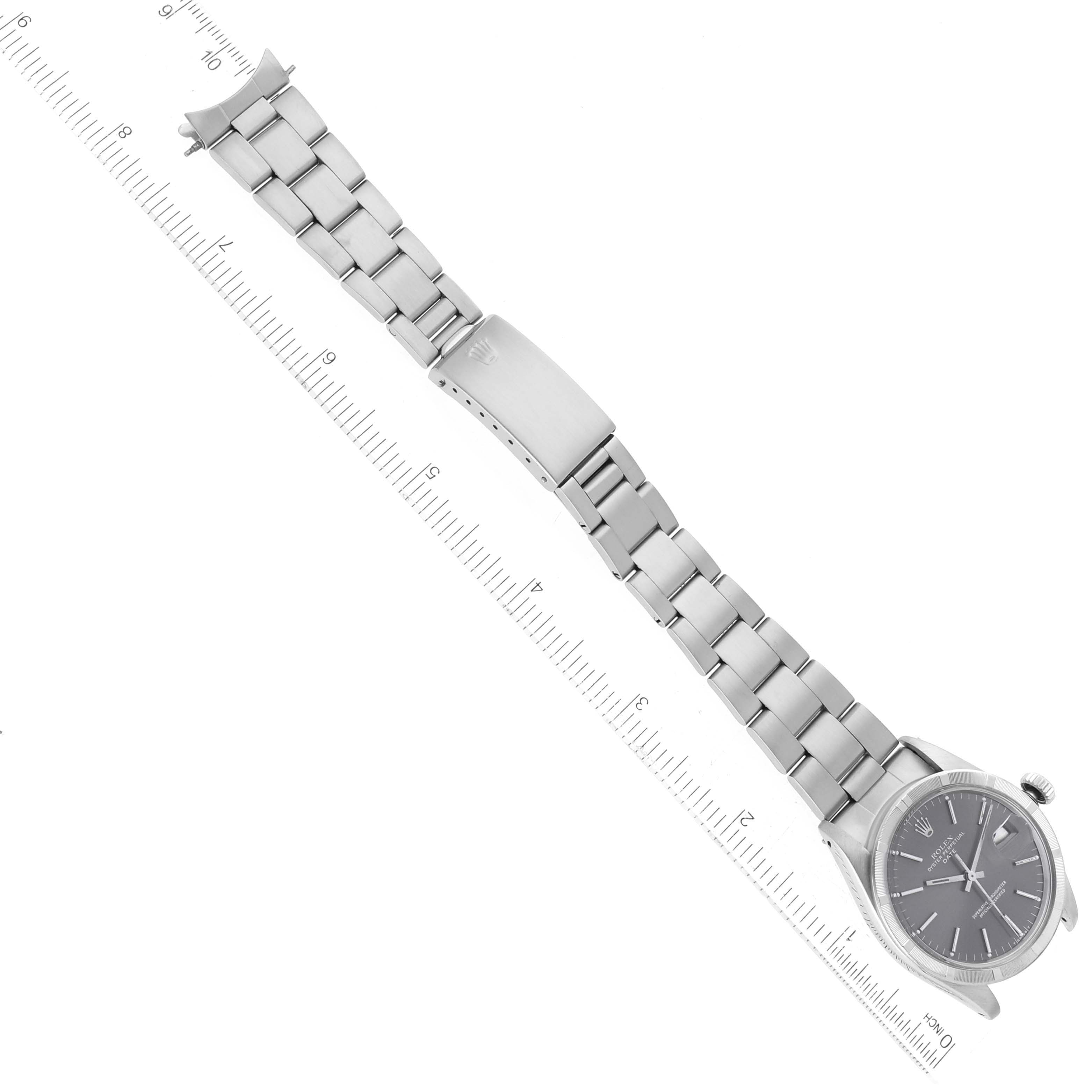 The image shows a full view of a Rolex Date 1501 Men
s Stainless Steel Grey Dial 1501 Men
s Stainless Steel Grey Dial model watch, featuring its bracelet, clasp, and watch face, aligned next to a ruler.