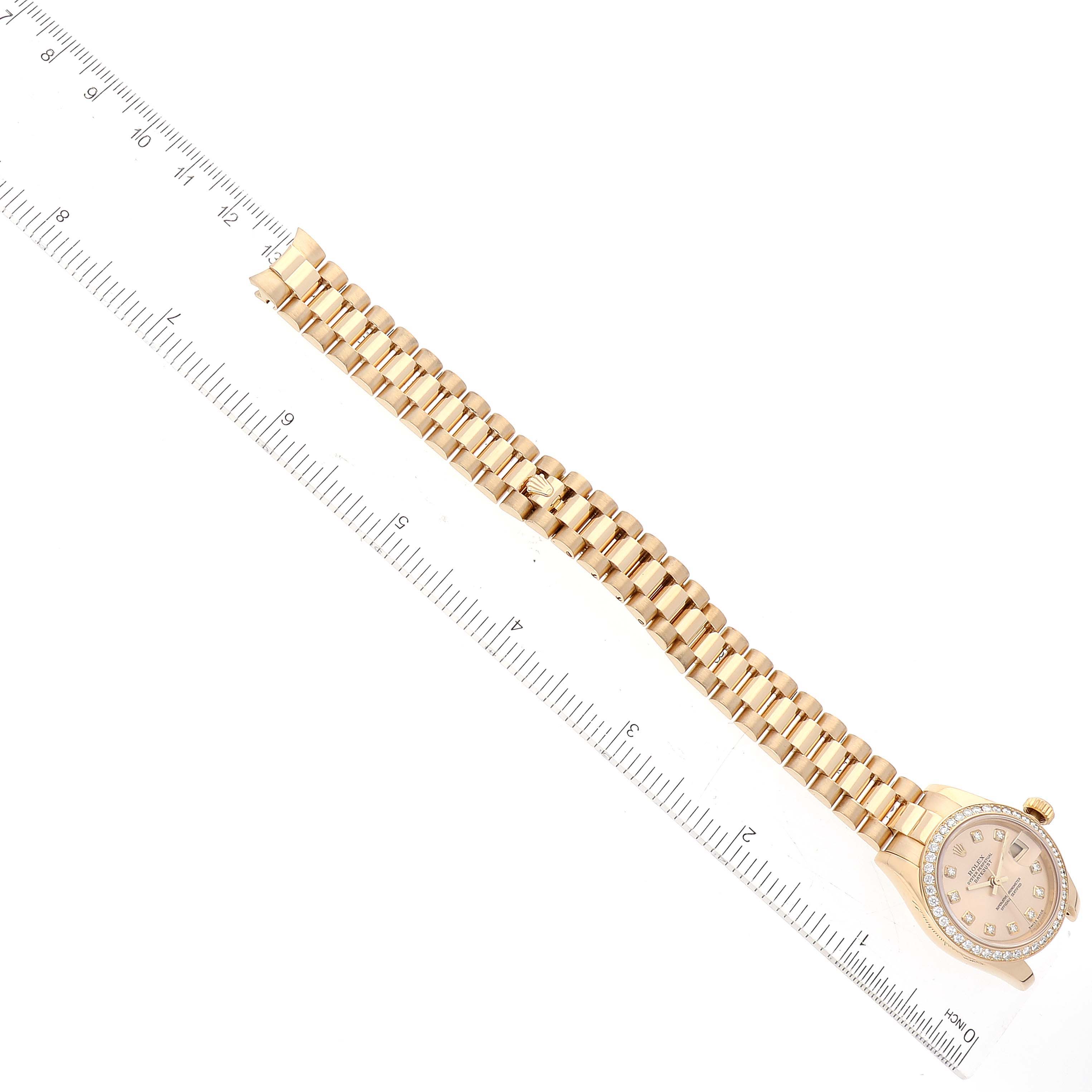 The image shows a Rolex President 179178 Women
s Yellow Gold Champagne Dial 179178 Women
s Yellow Gold Champagne Dial model watch lying flat with a ruler alongside, highlighting the watch face and full bracelet.