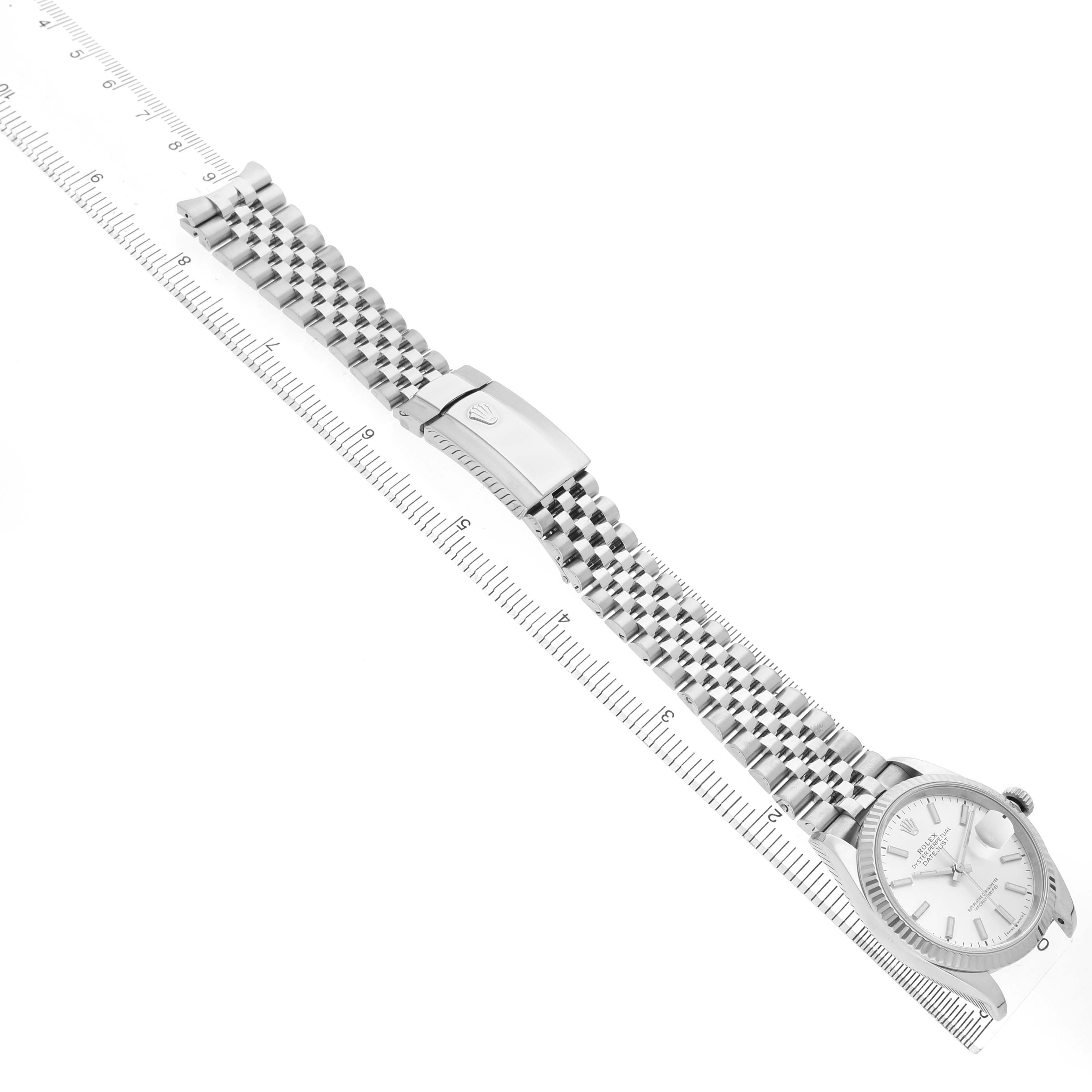 The Rolex Datejust MENS Men's Stainless Steel Silver Dial watch is shown from an angled side view, displaying the face, bracelet, and clasp next to a ruler.