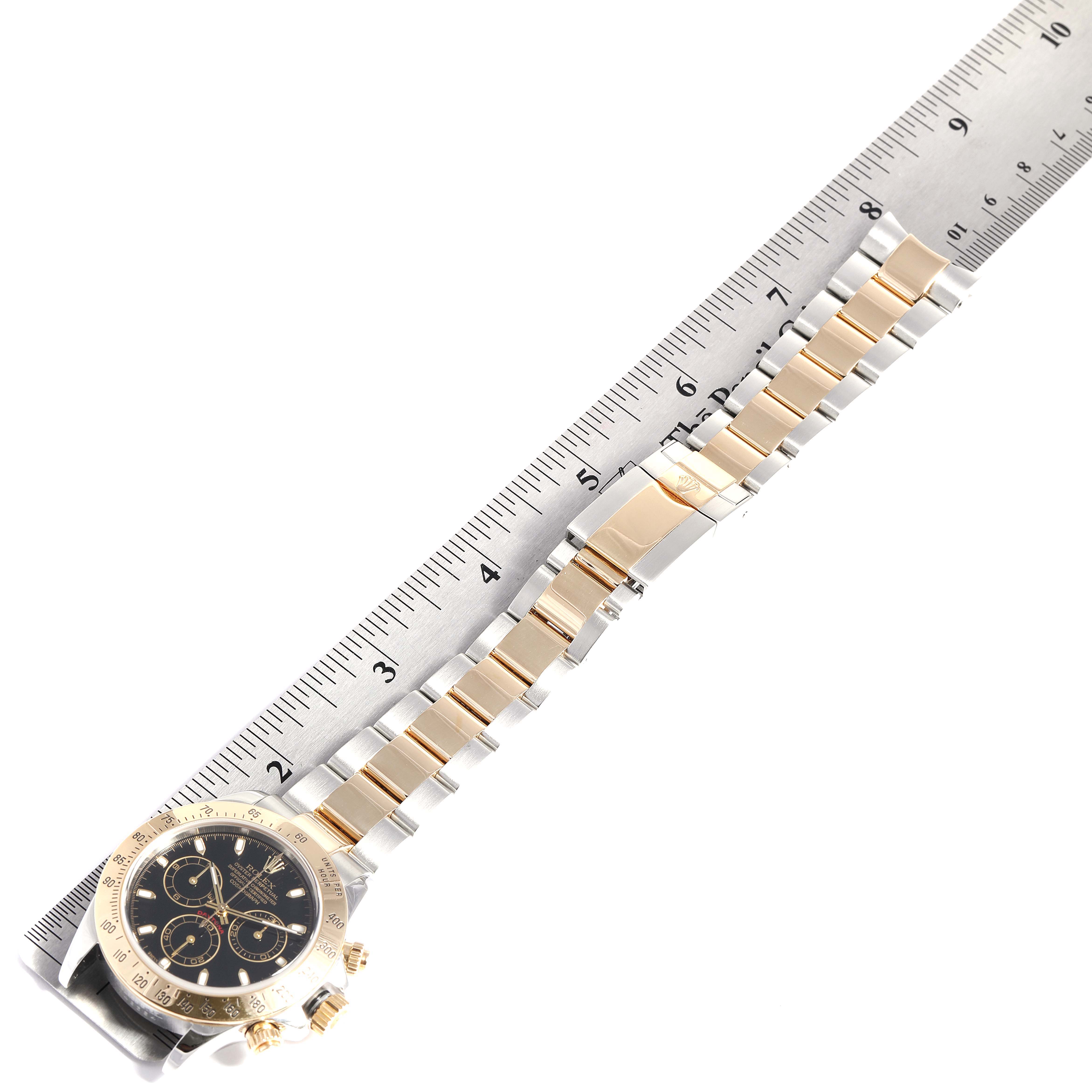 This image shows the Rolex Daytona 116523 Men
s Steel and Gold (two tone) Black Dial 116523 Men
s Steel and Gold (two tone) Black Dial watch horizontally next to a ruler, showcasing its band and clasp.