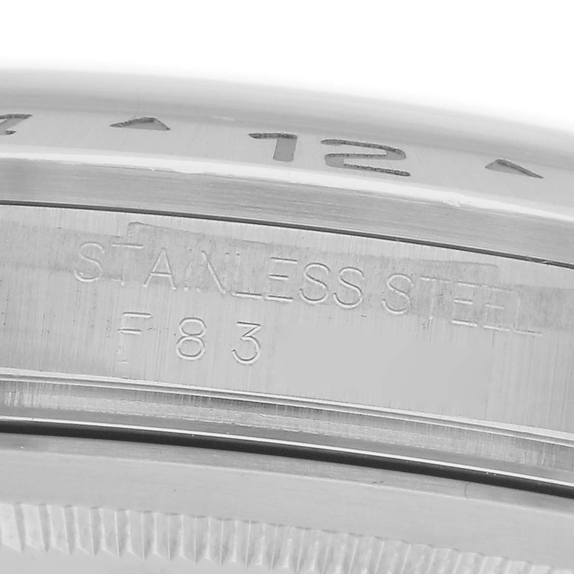 The image shows a close-up of the bezel and part of the case, highlighting the "STAINLESS STEEL" engraving on the Rolex Explorer model 216570.