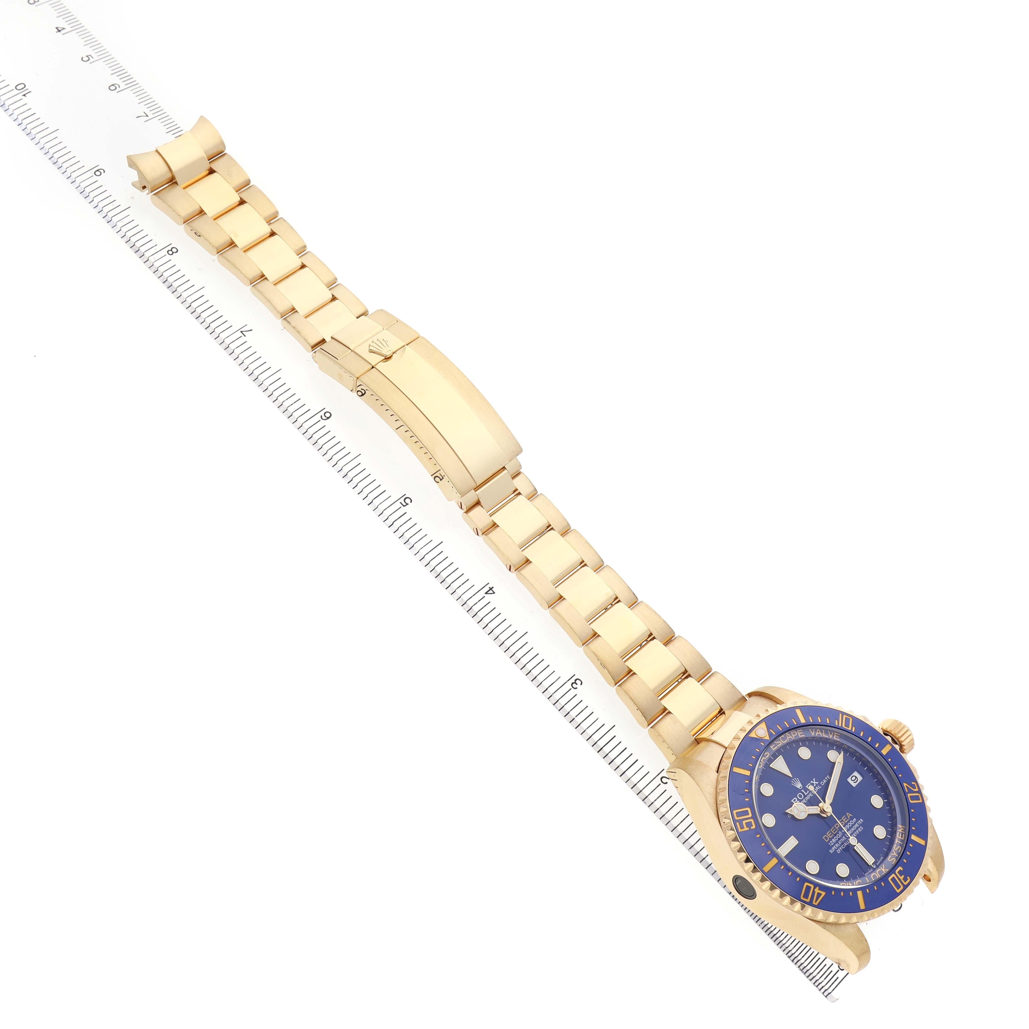 The Rolex Sea-Dweller 136668LB Men's Yellow Gold Blue Dial watch is shown at an angled top view, highlighting the blue dial, bezel, and gold bracelet aligned with a ruler.