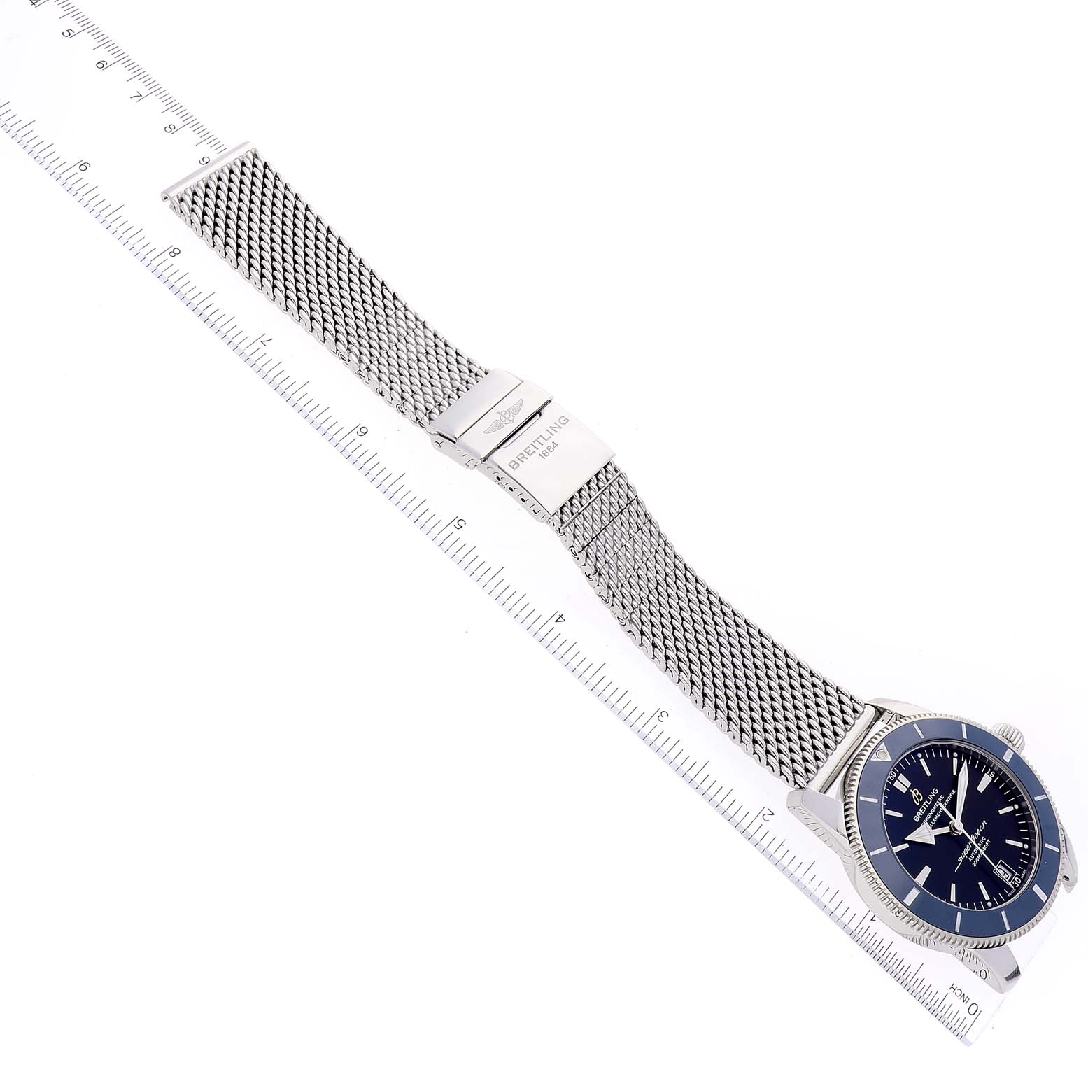 The image shows a top-down view of a Breitling Superocean AB2010 Men's Stainless Steel Black Dial AB2010 Men's Stainless Steel Black Dial watch with a mesh band next to a ruler for measurement.