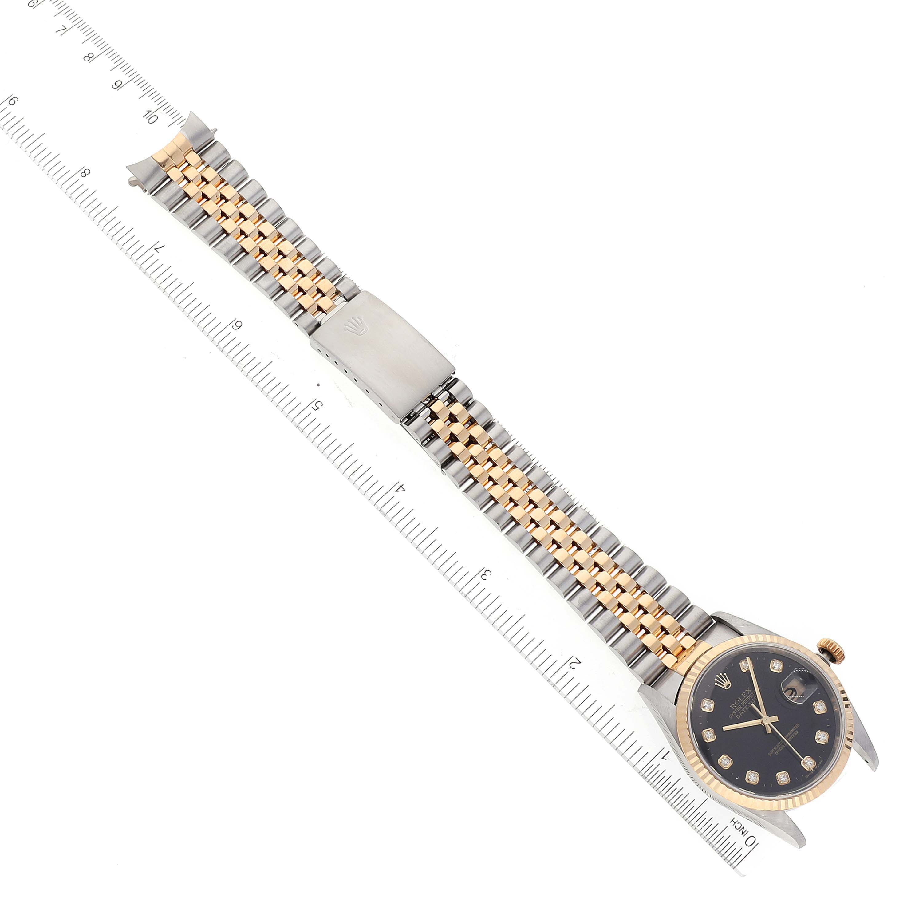 The image shows a Rolex Datejust 16233 Men
s Steel and Gold (two tone) Black Dial 16233 Men
s Steel and Gold (two tone) Black Dial watch laid flat, featuring its dial, bezel, and bracelet alongside a ruler for size reference.