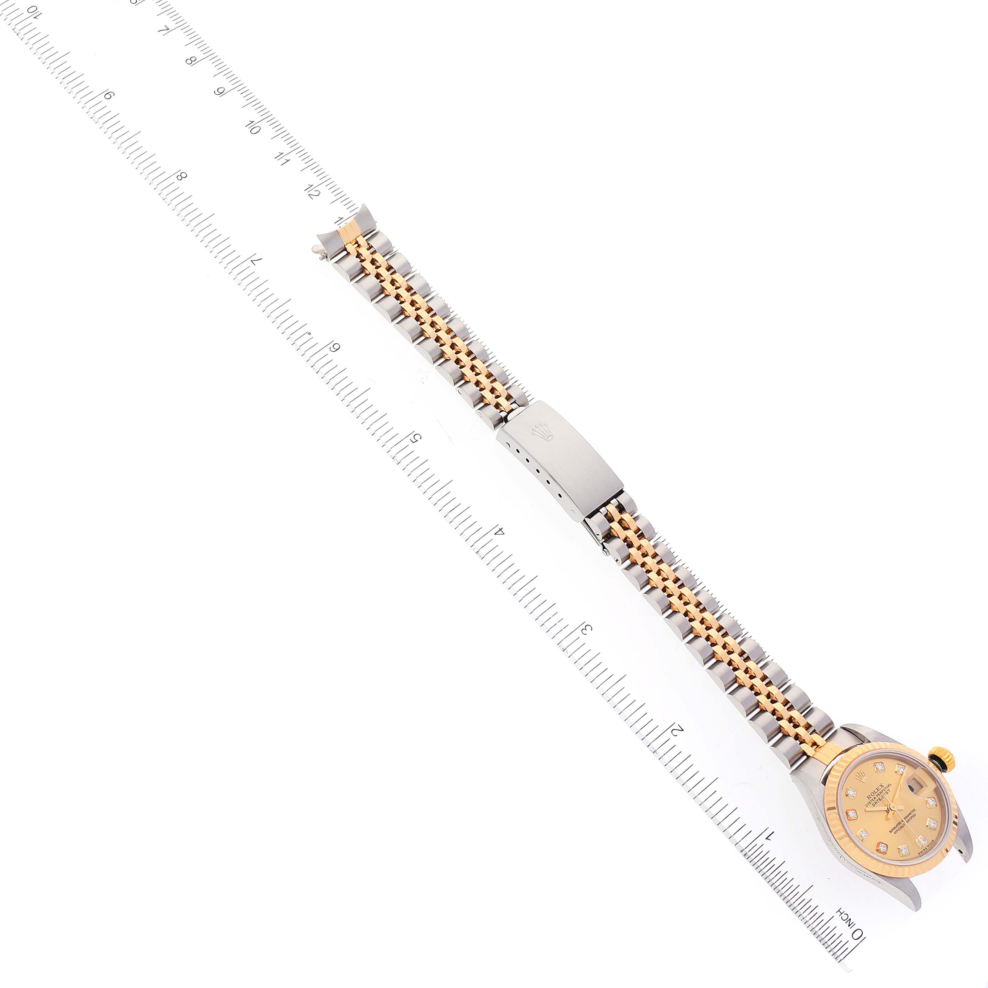 The Rolex Datejust 79173 Women
s Steel and Gold (two tone) Champagne Dial 79173 Women
s Steel and Gold (two tone) Champagne Dial watch is shown from a top-down angle alongside a measuring ruler, displaying the face, strap, and clasp.