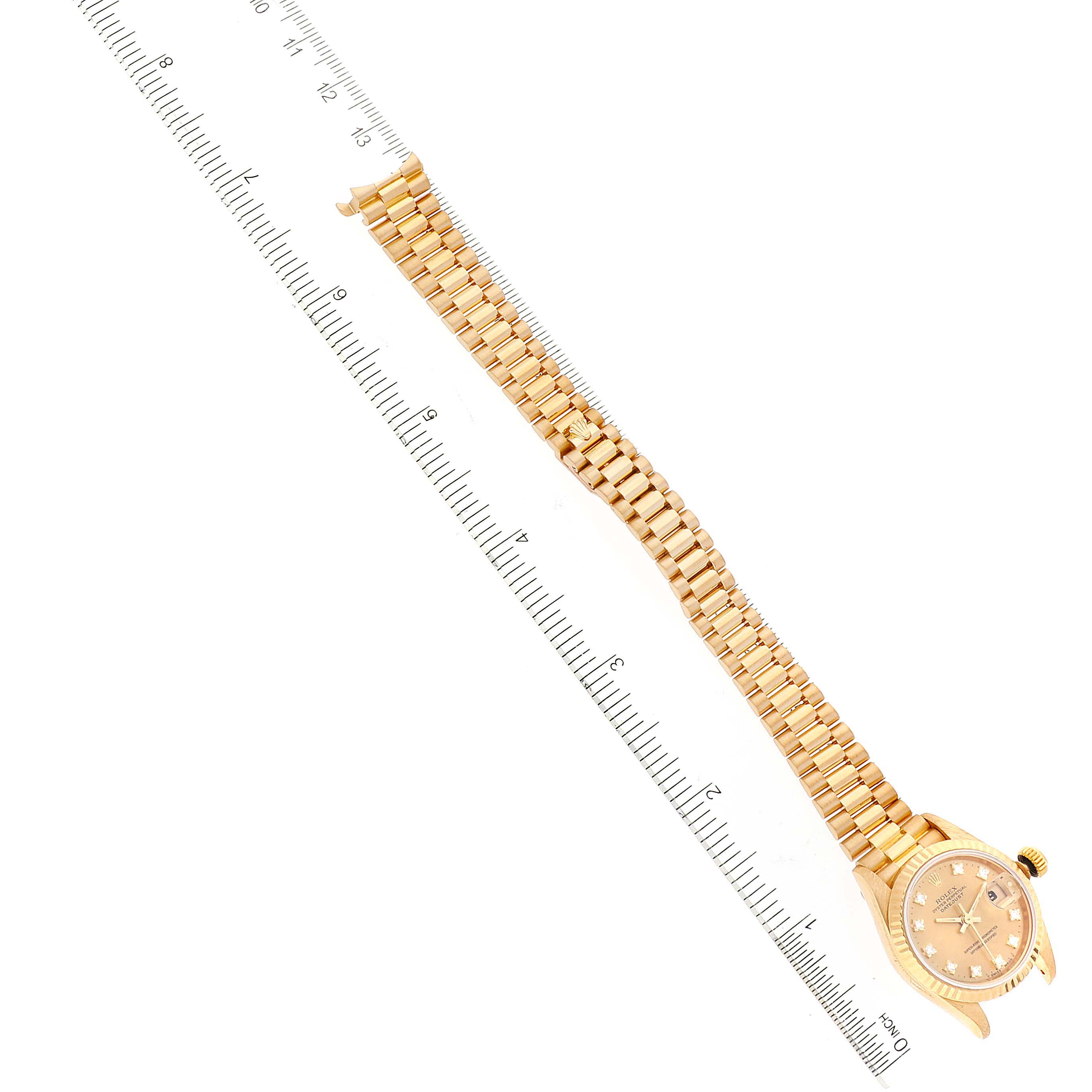 The image shows a Rolex President 69178 Women
s Yellow Gold Champagne Dial 69178 Women
s Yellow Gold Champagne Dial watch laid flat at an angle with a ruler beside it for scale.