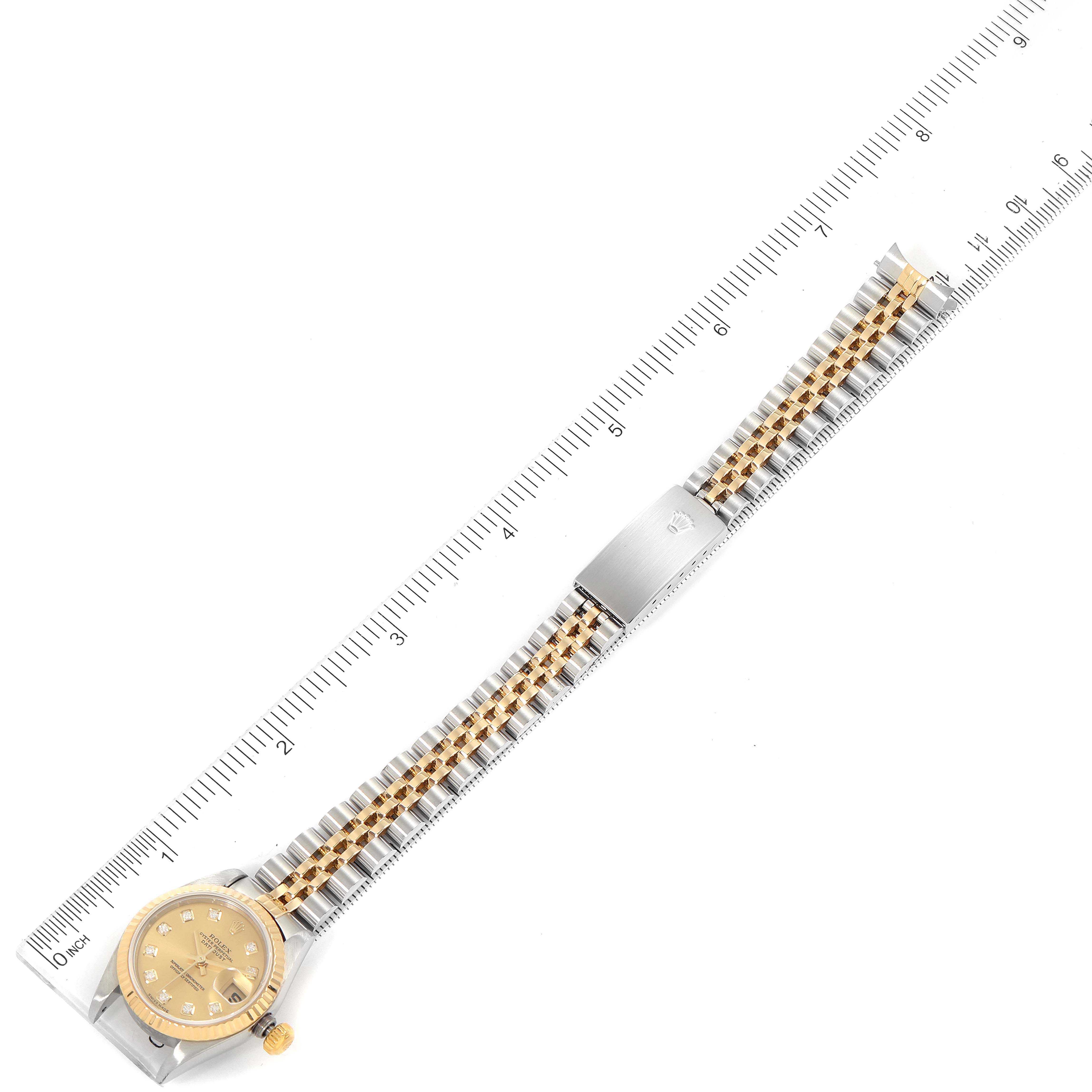 The image shows a Rolex Datejust 79173 Women
s Steel and Gold (two tone) Champagne Dial 79173 Women
s Steel and Gold (two tone) Champagne Dial watch laid flat with its bracelet fully extended next to a ruler.