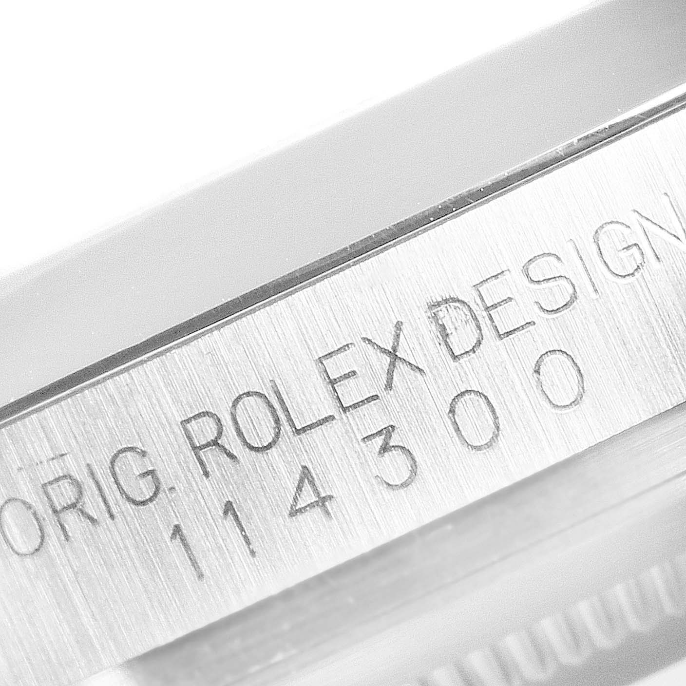 The image shows a close-up of the engraved side of a Rolex Oyster Perpetual 114300 Men's Stainless Steel Grey Dial watch case with model number details.