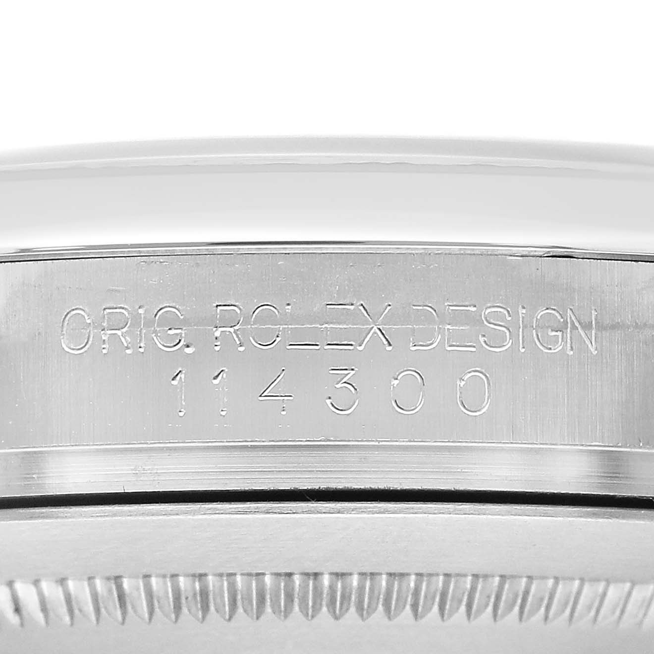 The image shows the side of a Rolex Oyster Perpetual 114300 Men's Stainless Steel Blue Dial watch, focusing on the engraved design number.