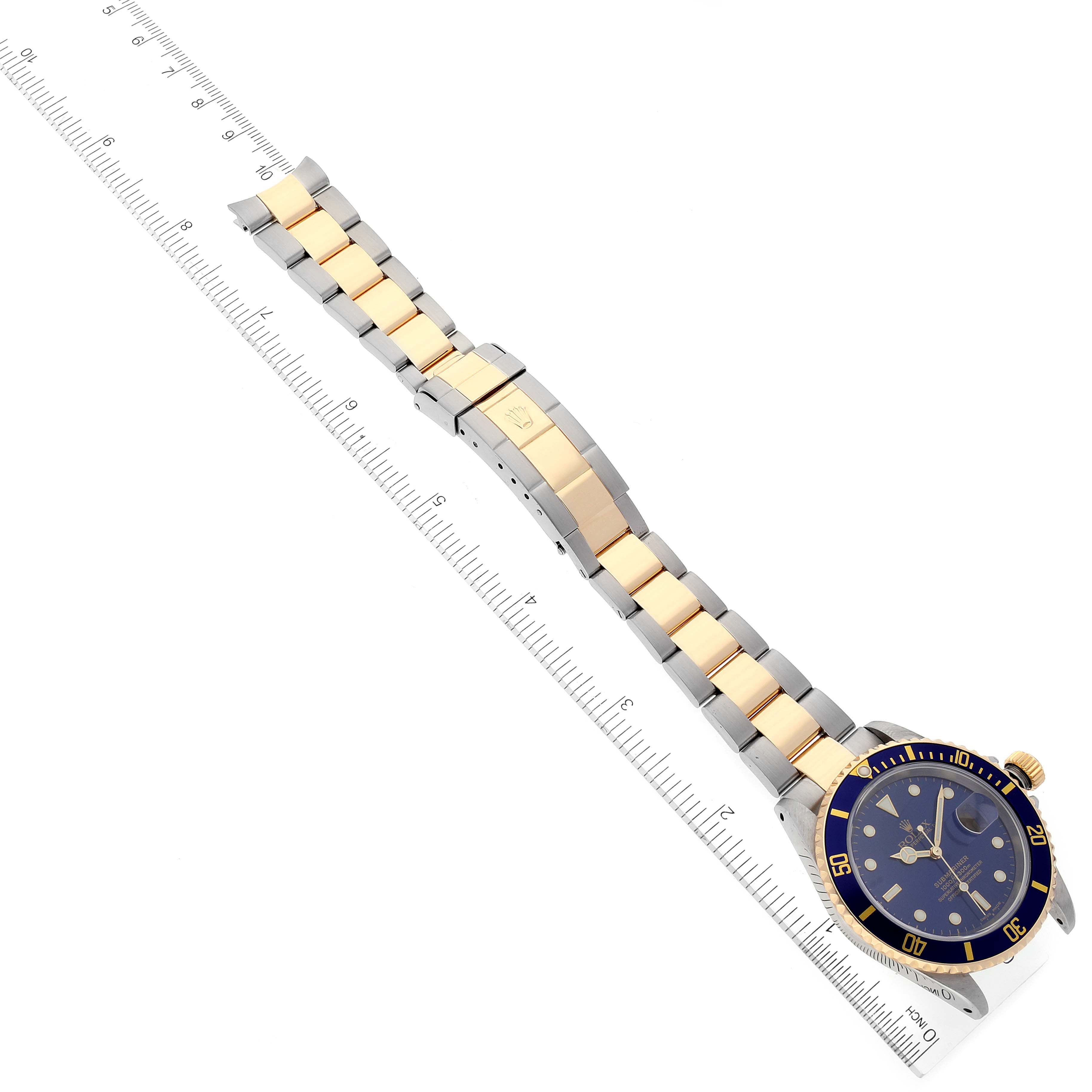 The Rolex Submariner 16613 Men's Steel and Gold (two tone) Blue Dial 16613 Men's Steel and Gold (two tone) Blue Dial watch is shown at an angled top-down view, displaying its bezel, dial, bracelet, and clasp next to a ruler.