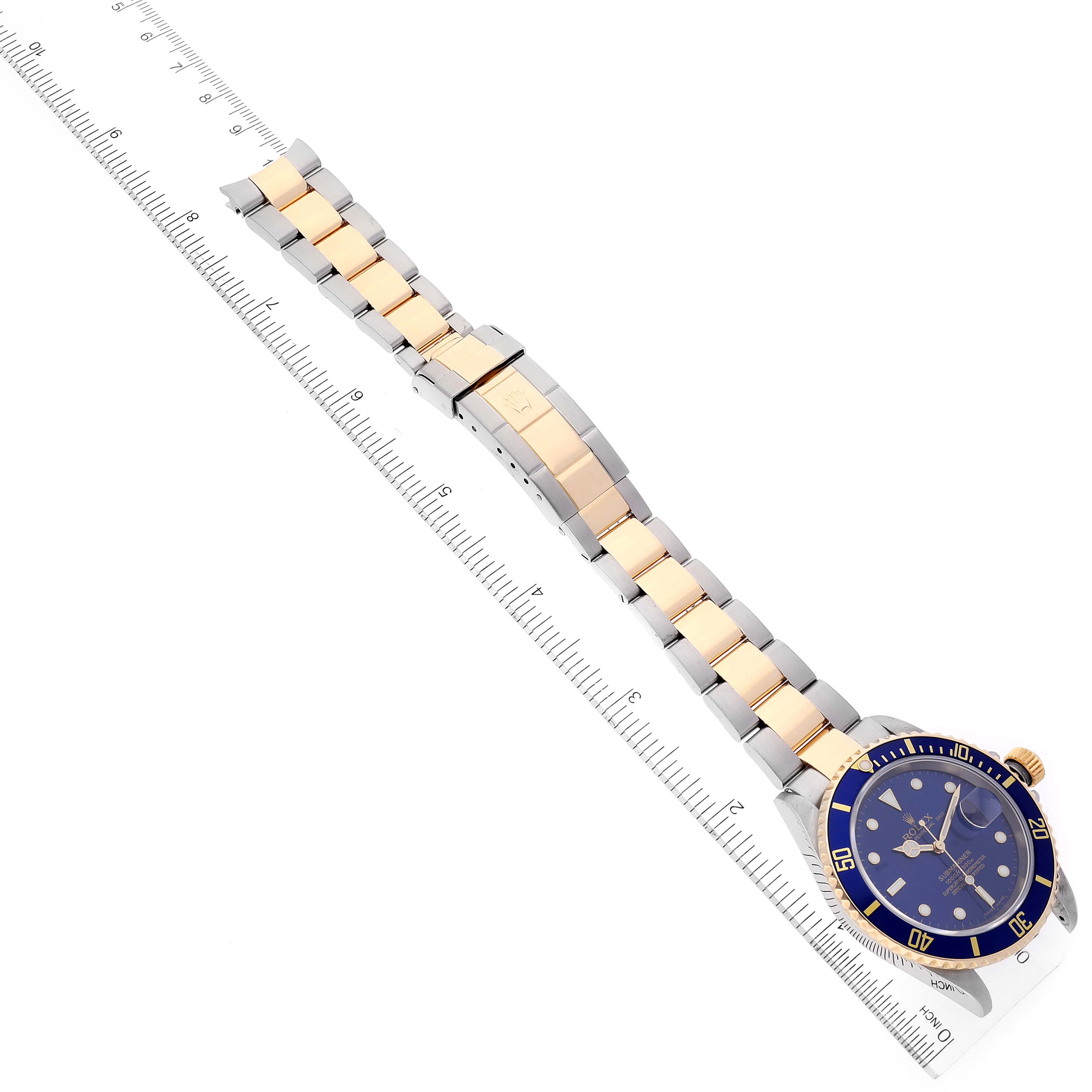 This image shows a Rolex Submariner 16613 Men
s Steel and Gold (two tone) Blue Dial 16613 Men
s Steel and Gold (two tone) Blue Dial watch laid flat with a ruler alongside, displaying the full bracelet and watch face.