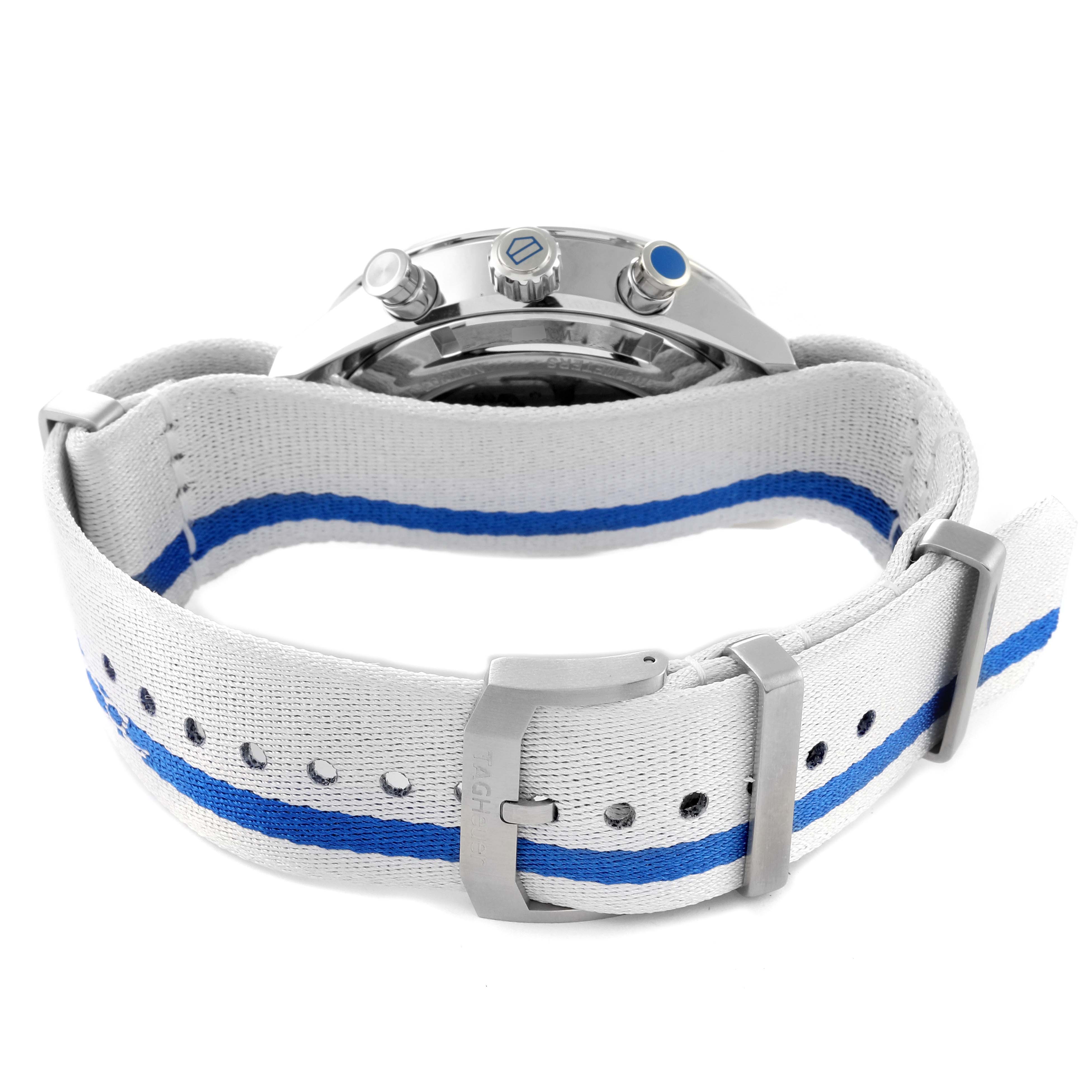 The image shows the back angle of a Tag Heuer Carrera watch with a white strap featuring a blue stripe and metal buckle.