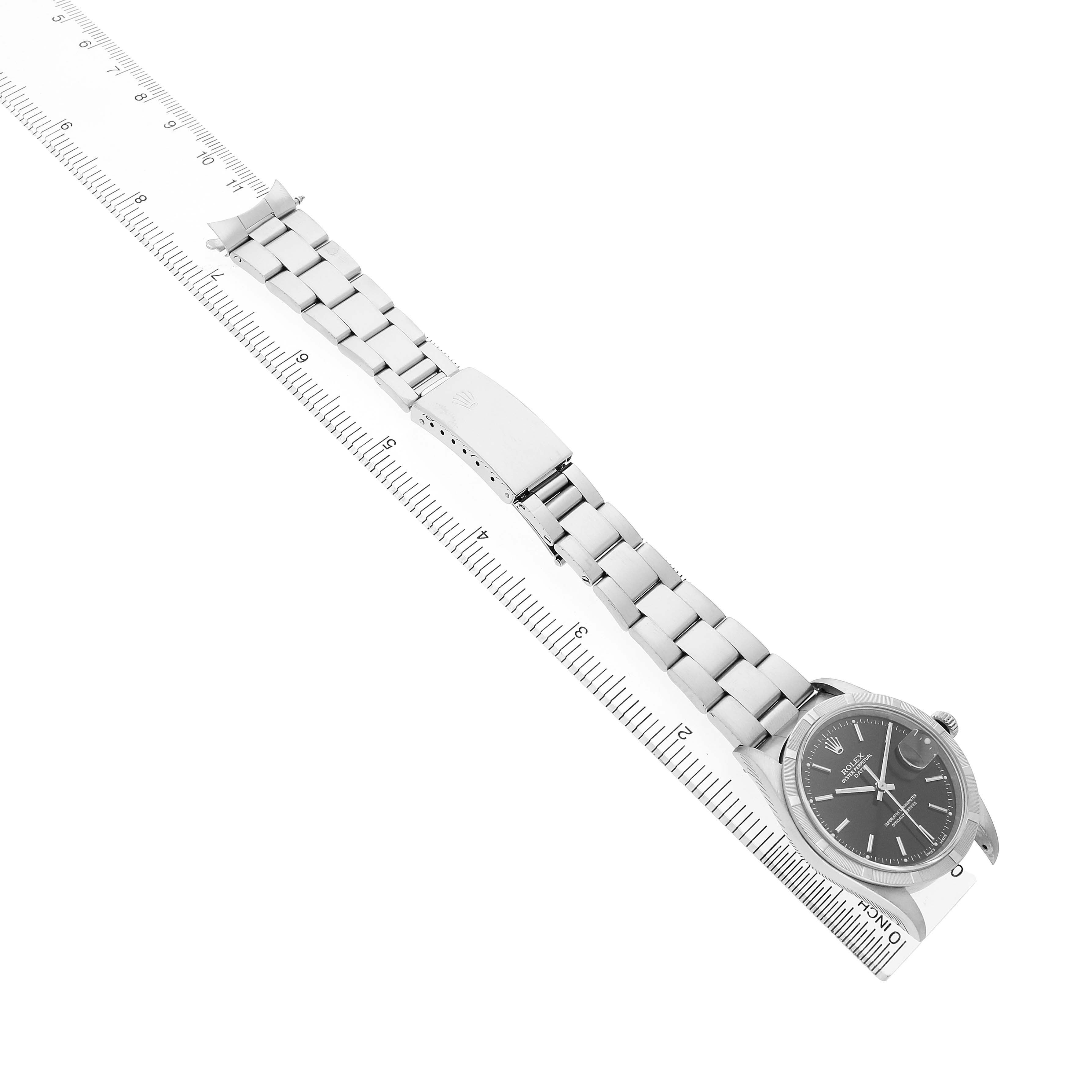 The Rolex Date 15210 Men's Stainless Steel Black Dial watch is shown from a top-down angle, displaying its face, bracelet, and clasp, aligned with a ruler.