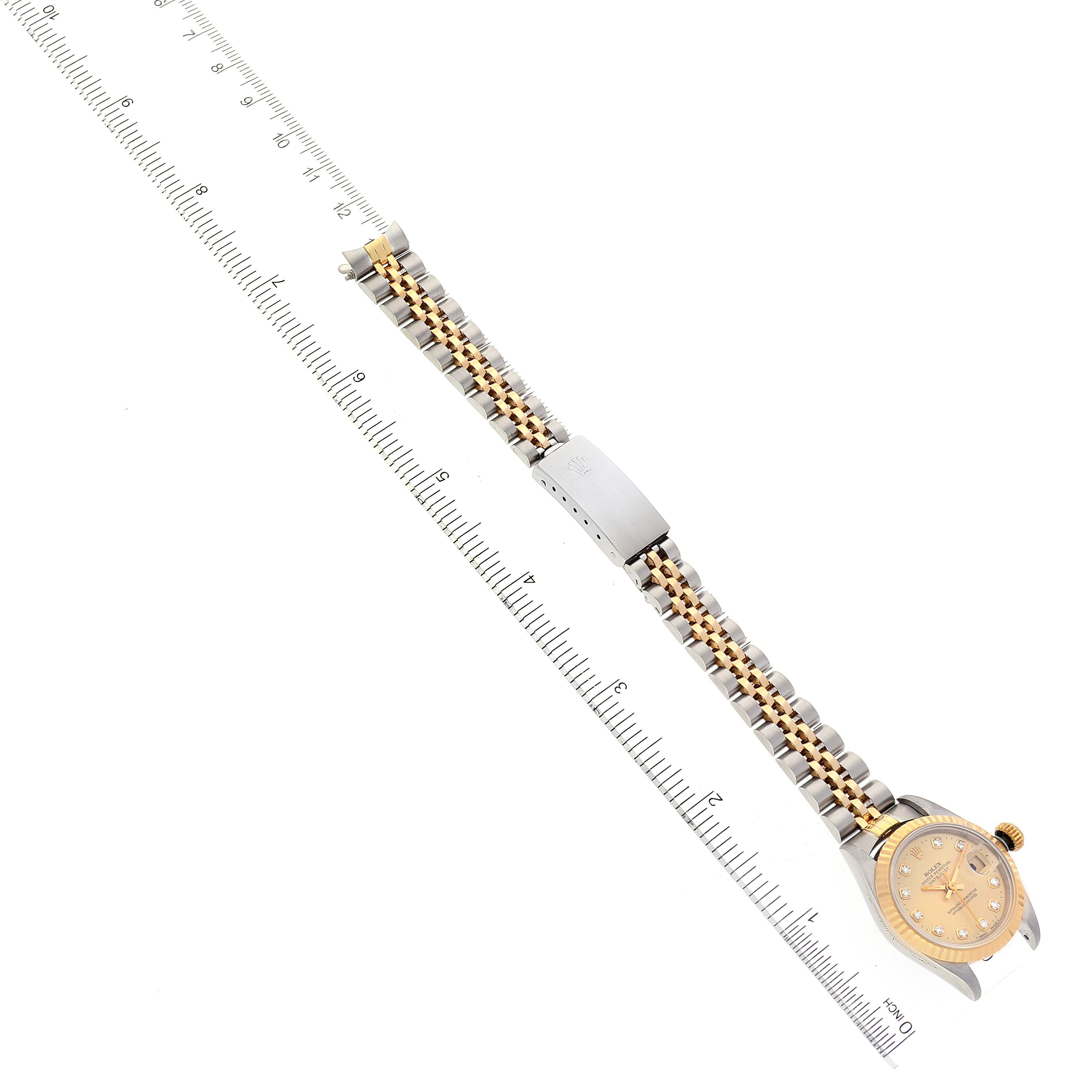 The image shows a Rolex Datejust 69173 Women
s Steel and Gold (two tone) Champagne Dial 69173 Women
s Steel and Gold (two tone) Champagne Dial watch laid flat with its dial and bracelet fully extended next to a measuring scale.