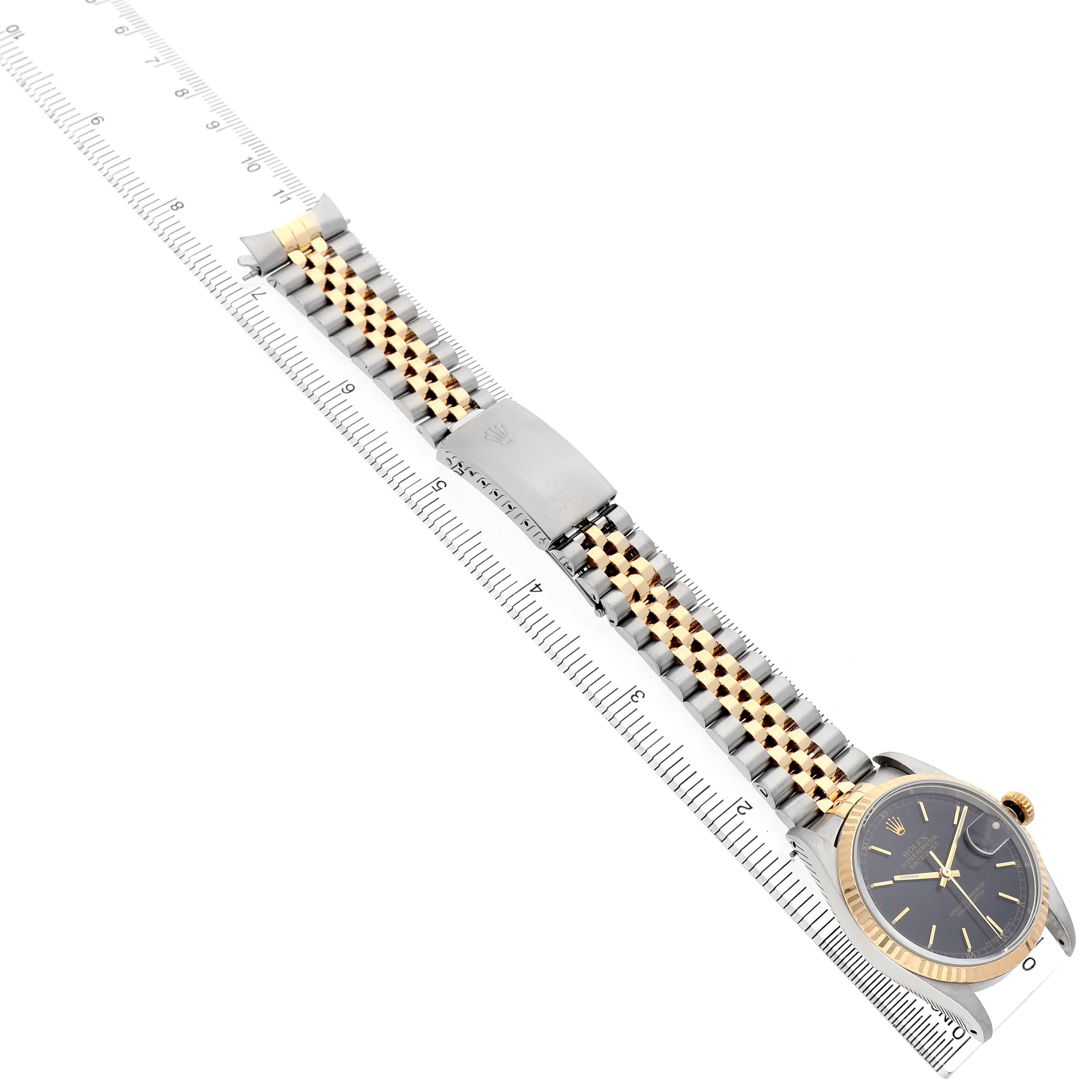 The Rolex Datejust 16233 Men's Steel and Gold (two tone) Black Dial watch is shown from a top angle, featuring its face, bezel, and Jubilee bracelet aligned with a ruler.