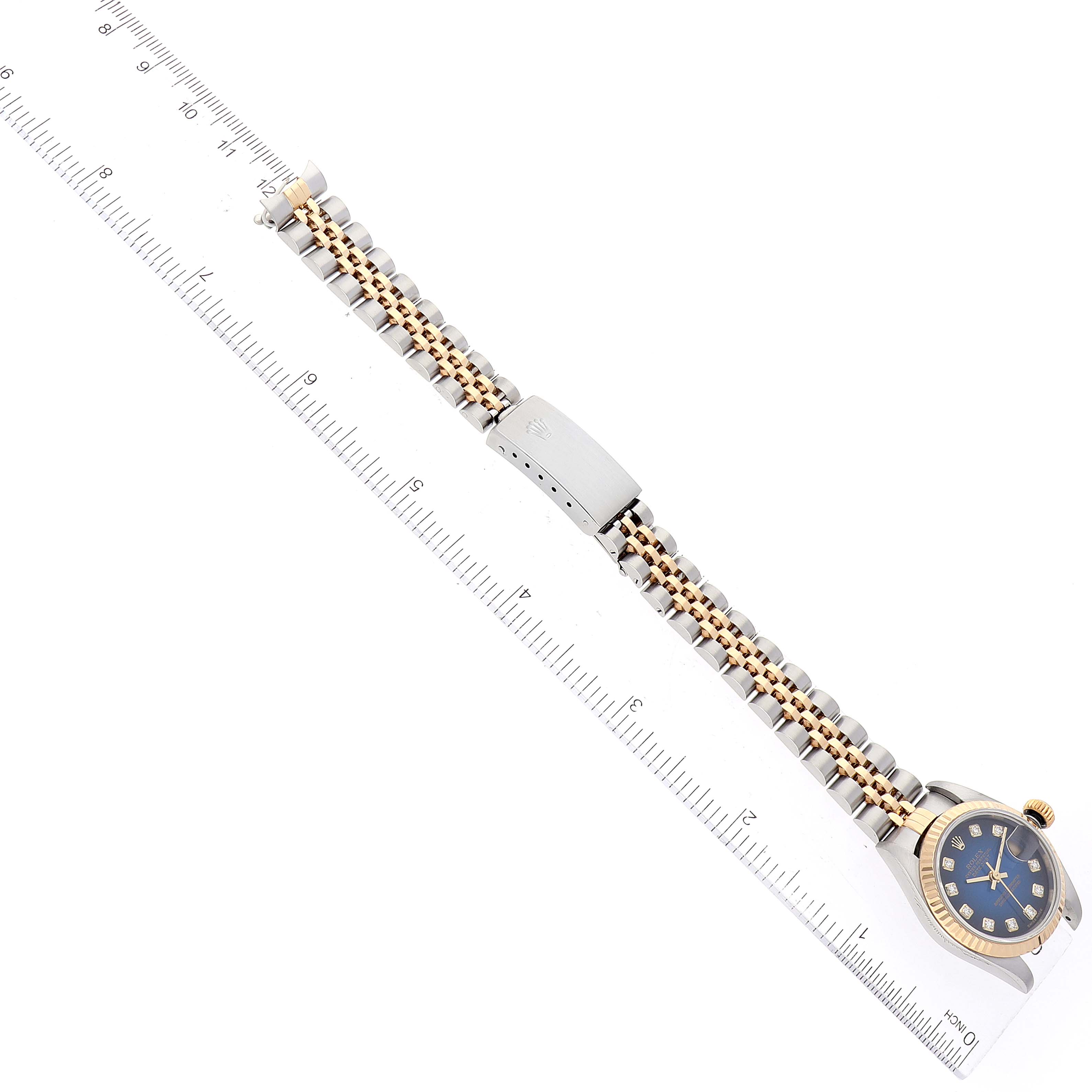 The image shows the Rolex Datejust 79173 Women's Steel and Gold (two tone) Blue Dial 79173 Women's Steel and Gold (two tone) Blue Dial watch horizontally, with focus on its bracelet, clasp, and part of the case, next to a ruler.