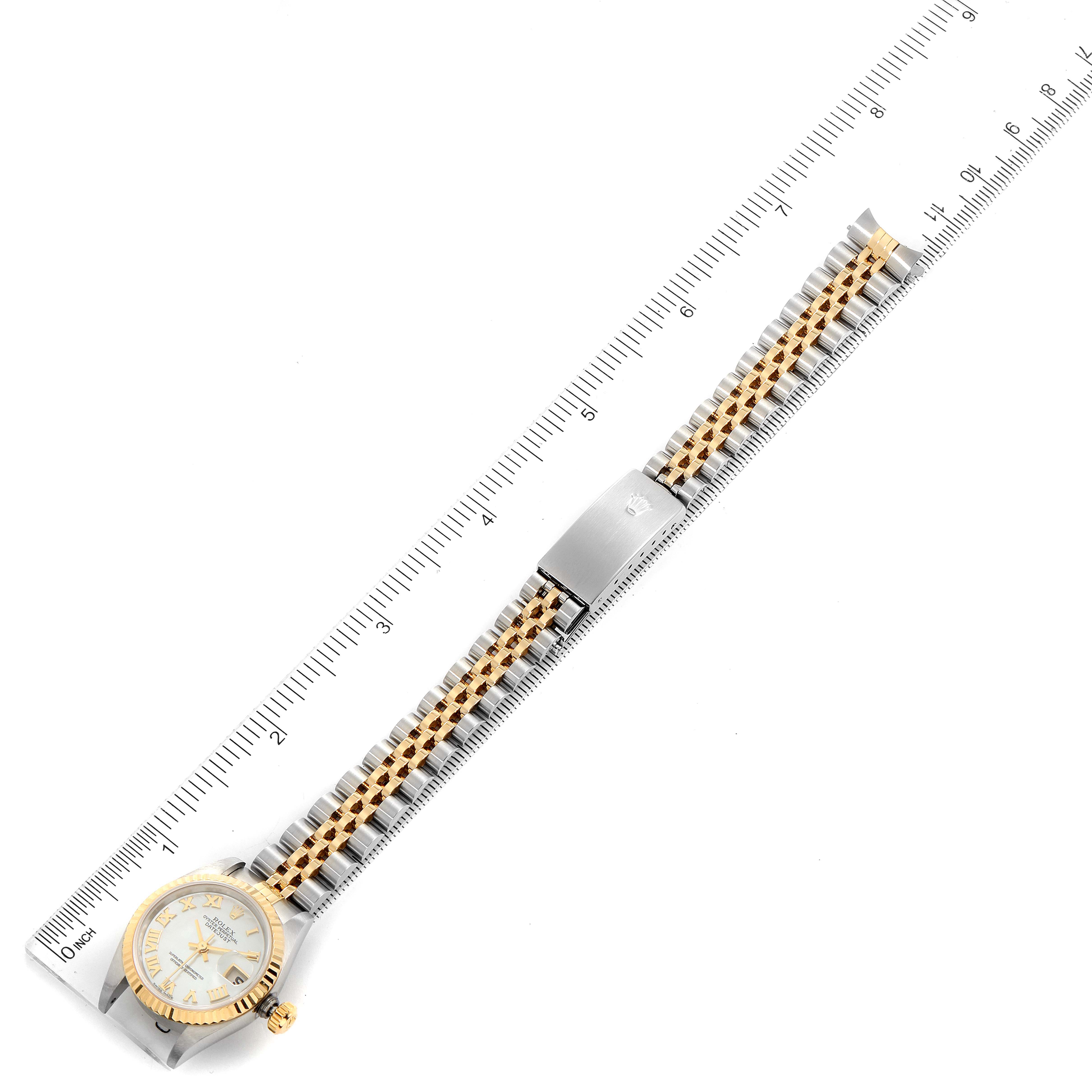 This image shows a Rolex Datejust 79173 Women's Steel and Gold (two tone) Mother of Pearl Dial 79173 Women's Steel and Gold (two tone) Mother of Pearl Dial watch laid flat with a metal band and a measuring ruler beside it.