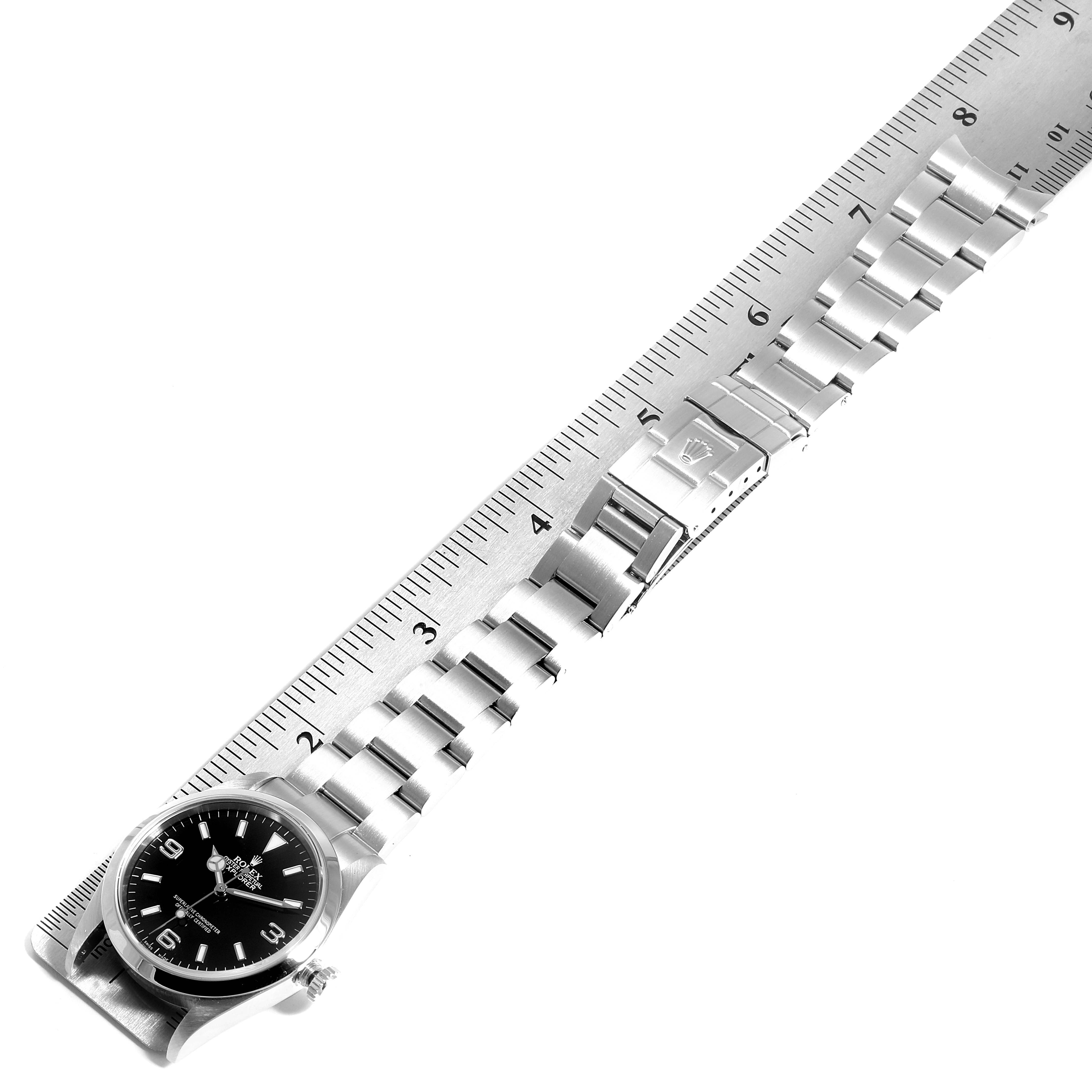 The image shows a Rolex Explorer 114270 Men
s Stainless Steel Black Dial 114270 Men
s Stainless Steel Black Dial watch at an angle, laying flat with a metal bracelet next to a ruler for scale.