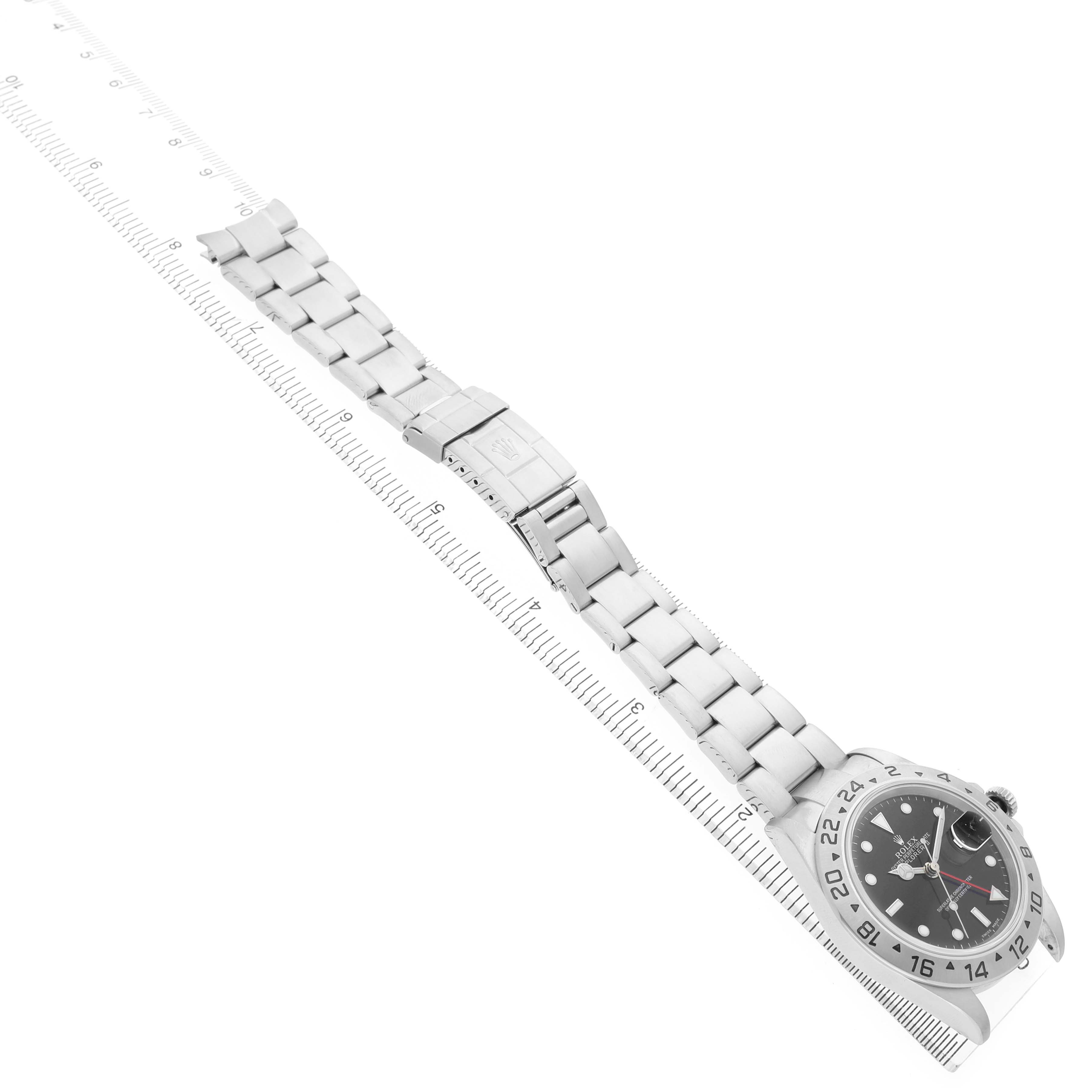 The Rolex Explorer 16570 Men's Stainless Steel Black Dial watch is shown from an angled top view, featuring its face, bezel, and full bracelet alongside a ruler.