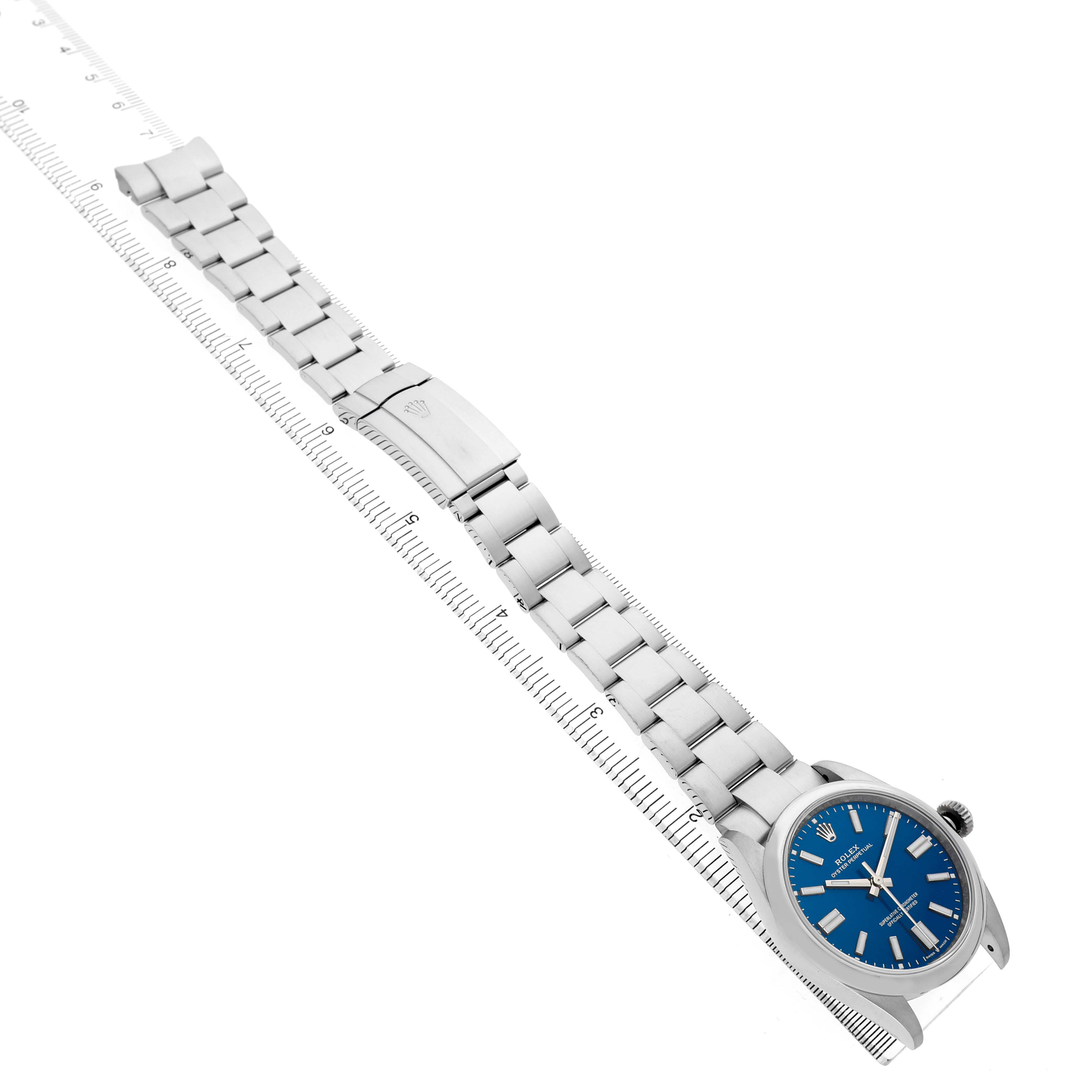 The image shows a Rolex Oyster Perpetual 134300 Men's Stainless Steel Blue Dial watch at a top-down angle, highlighting the face, bracelet, and clasp.