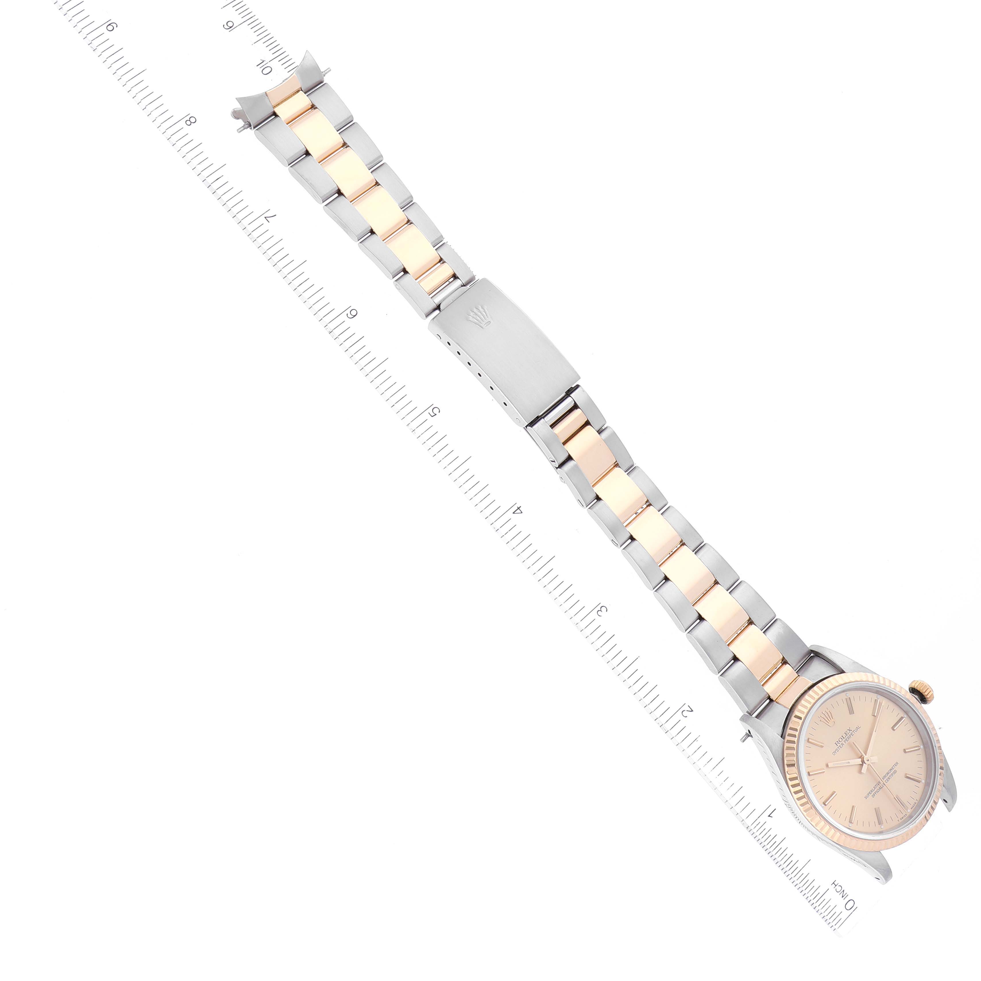 The Rolex Oyster Perpetual 14233 Men's Steel and Gold (two tone) Champagne Dial 14233 Men's Steel and Gold (two tone) Champagne Dial watch is shown from an overhead angle, displaying its bracelet, dial, clasp, and a ruler for scale.