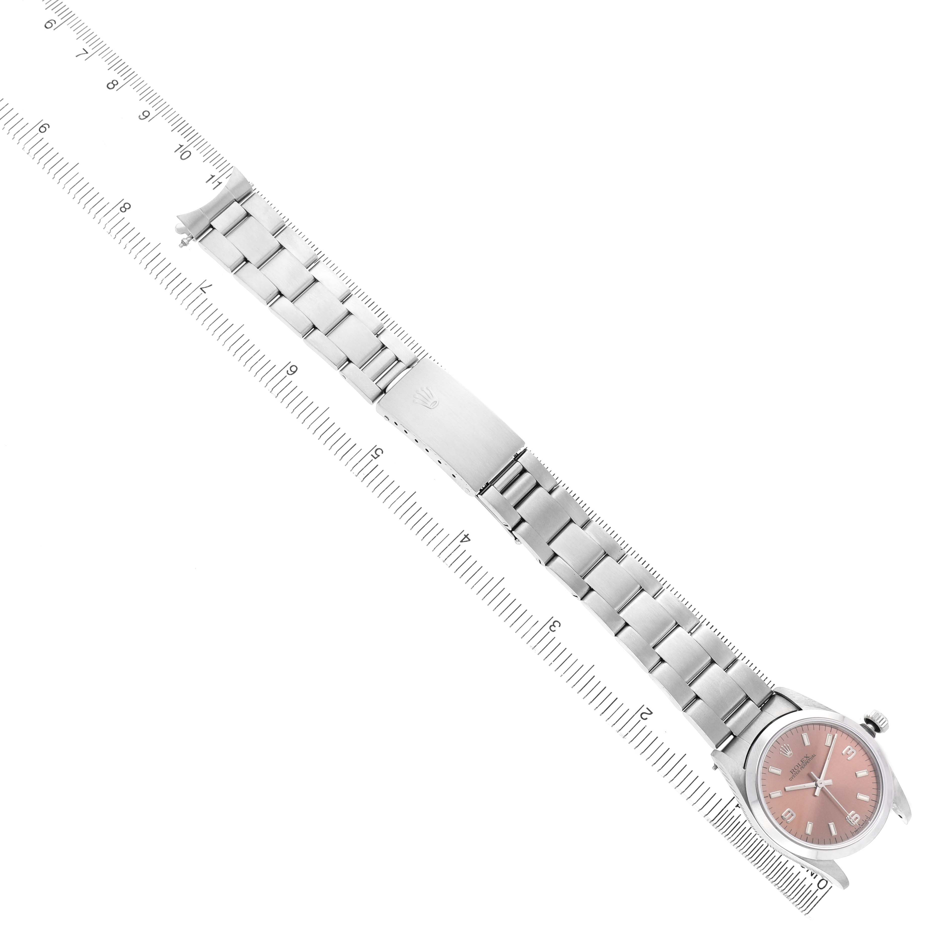 The Rolex Mid-Size 67480 Women's Stainless Steel Pink Dial model watch is shown from a top view, displaying the face, bracelet, and clasp alongside a ruler.