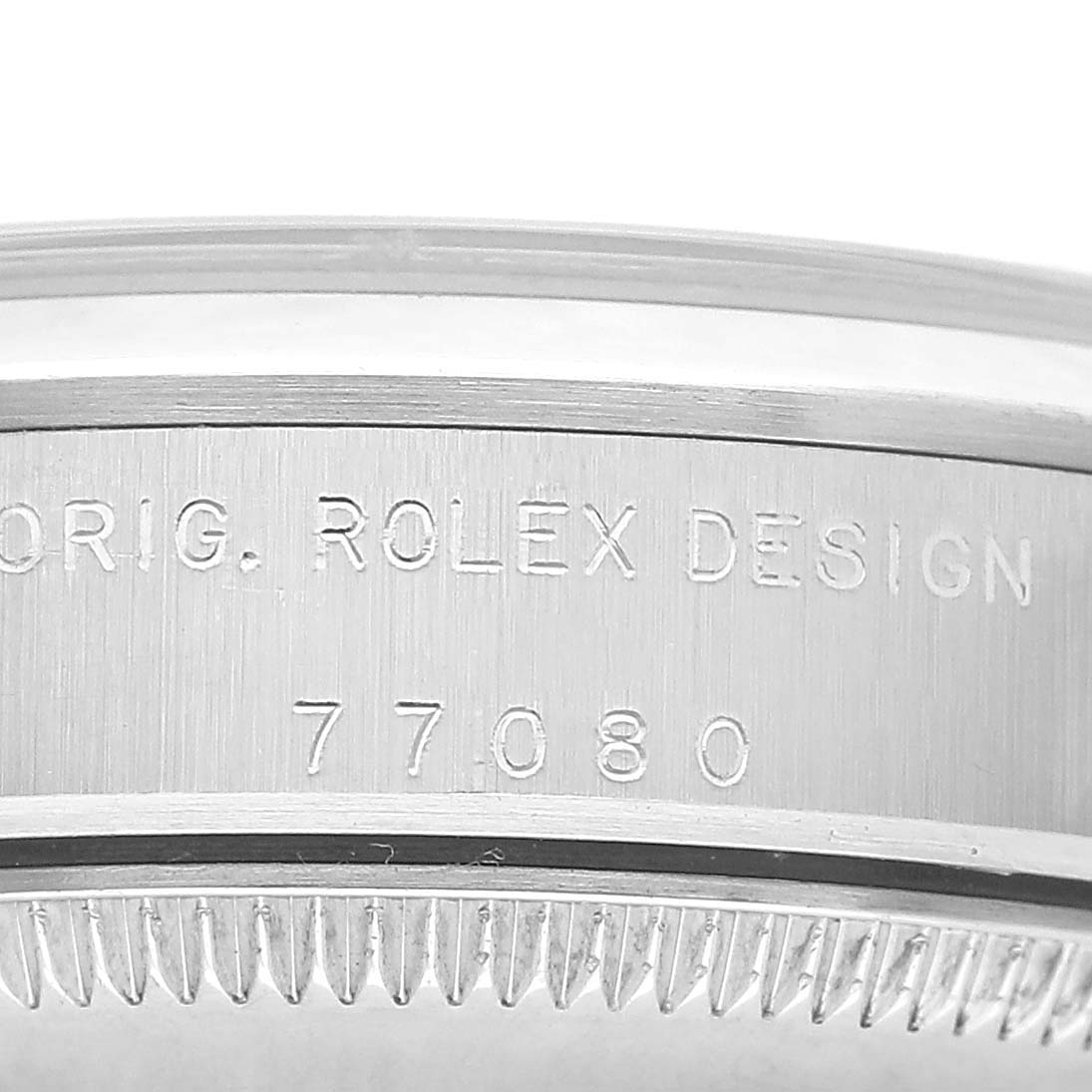 The image shows a close-up of the side of a Rolex Oyster Perpetual 77080 Women's Stainless Steel Silver Dial, highlighting the engraved "ORIG. ROLEX DESIGN" and a model number.