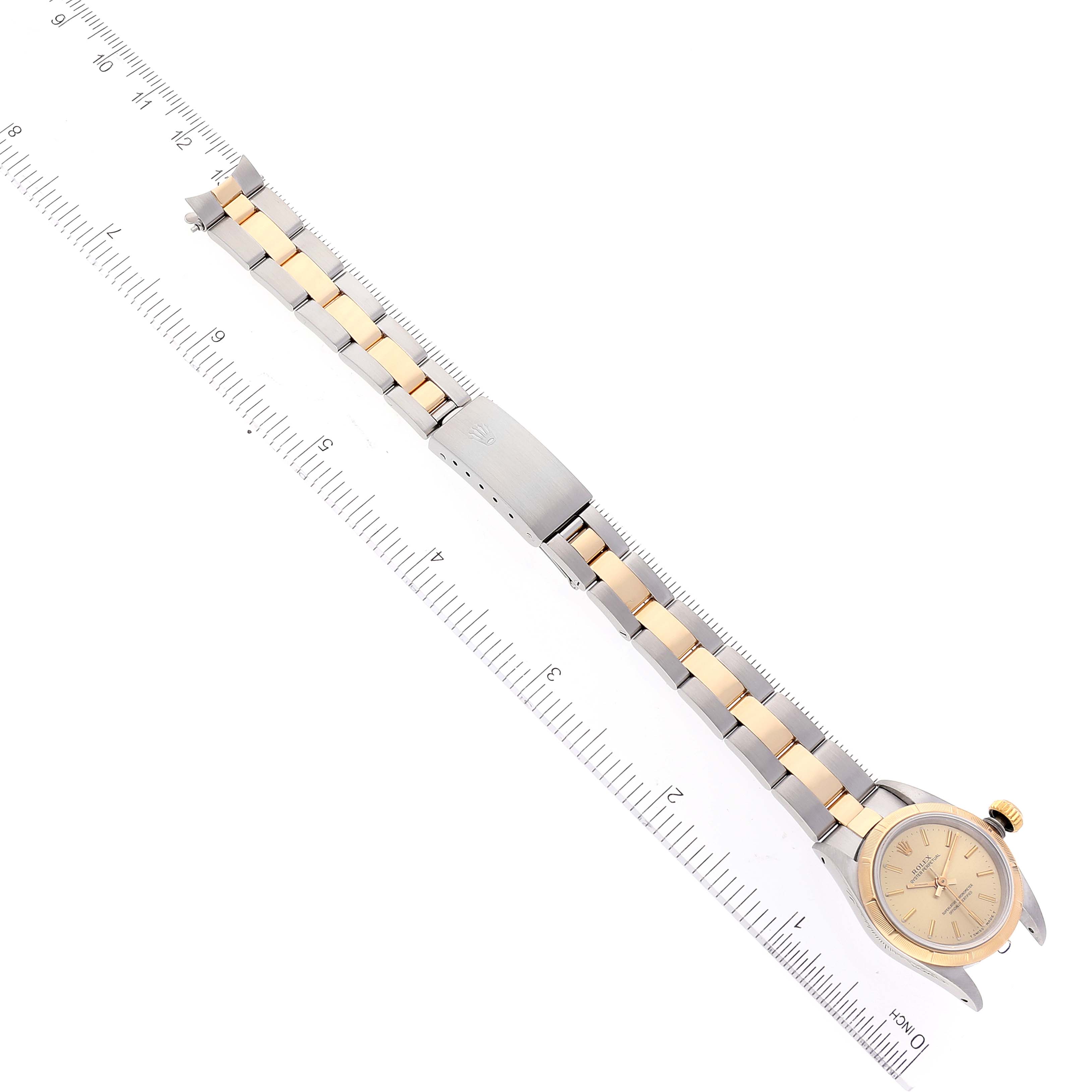 A Rolex Oyster Perpetual 67233 Women
s Steel and Gold (two tone) Champagne Dial 67233 Women
s Steel and Gold (two tone) Champagne Dial watch is shown laid flat, featuring the face, bezel, bracelet, and clasp alongside a ruler for measurement.