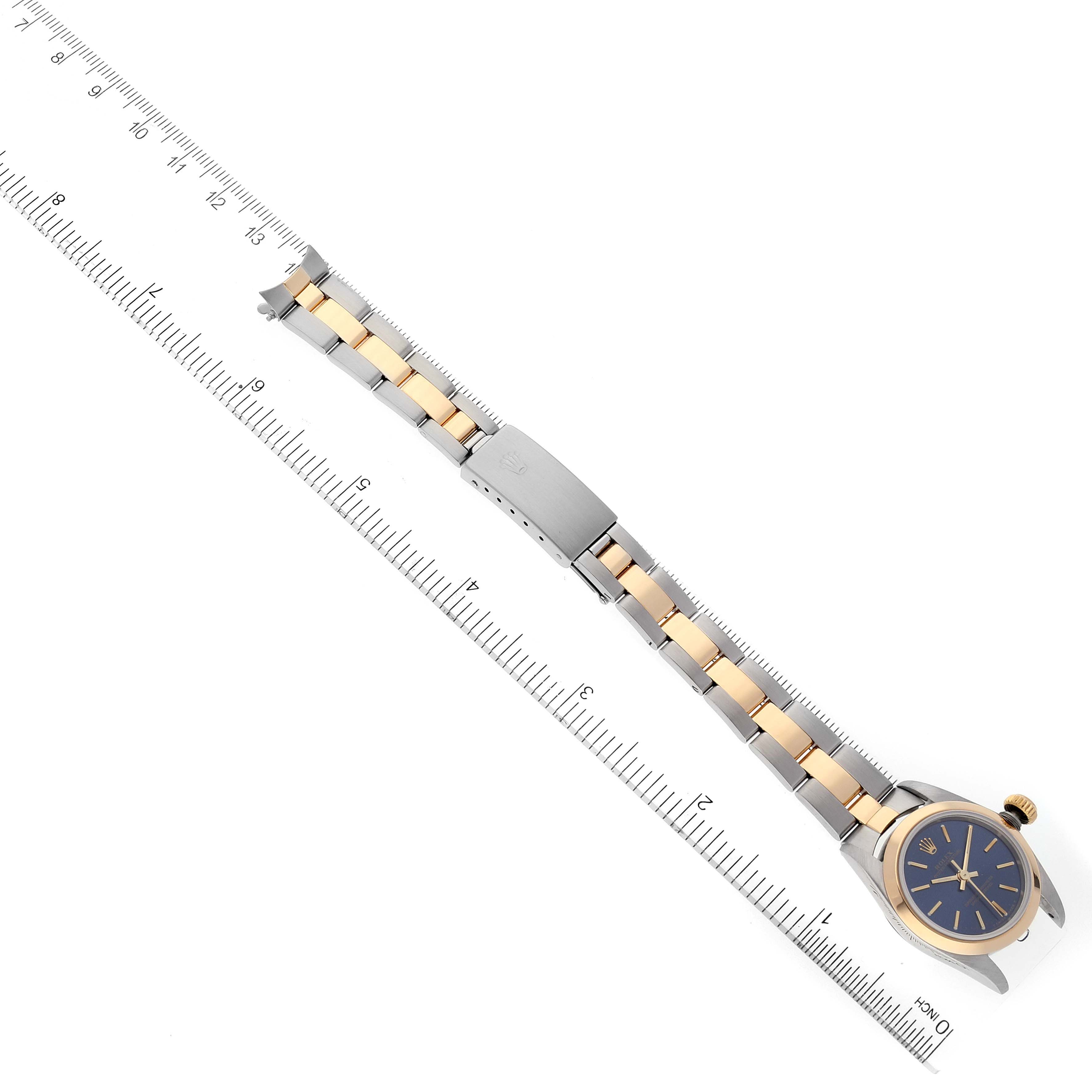 The image shows a Rolex Oyster Perpetual 67183 Women
s Steel and Gold (two tone) Blue Dial 67183 Women
s Steel and Gold (two tone) Blue Dial watch lying flat with its band extended next to a ruler for measurement.