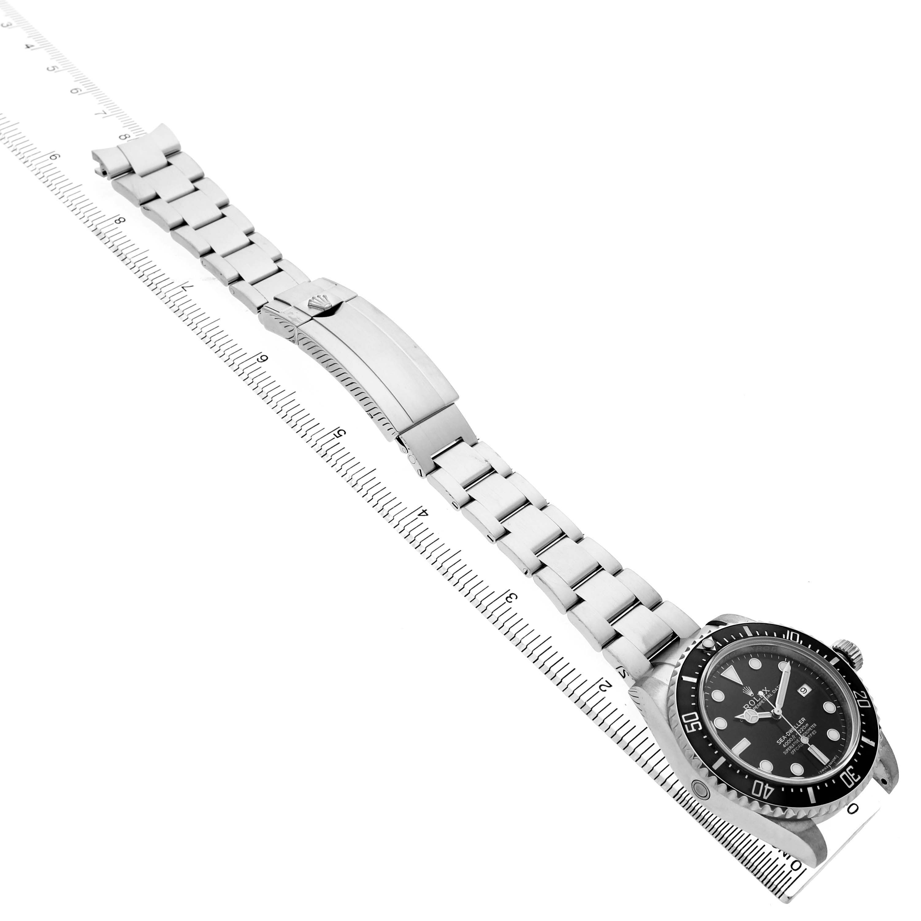The Rolex Sea-Dweller 116600 Men's Stainless Steel Black Dial watch is shown laid flat, highlighting its bracelet, clasp, and face, with a ruler for scale.