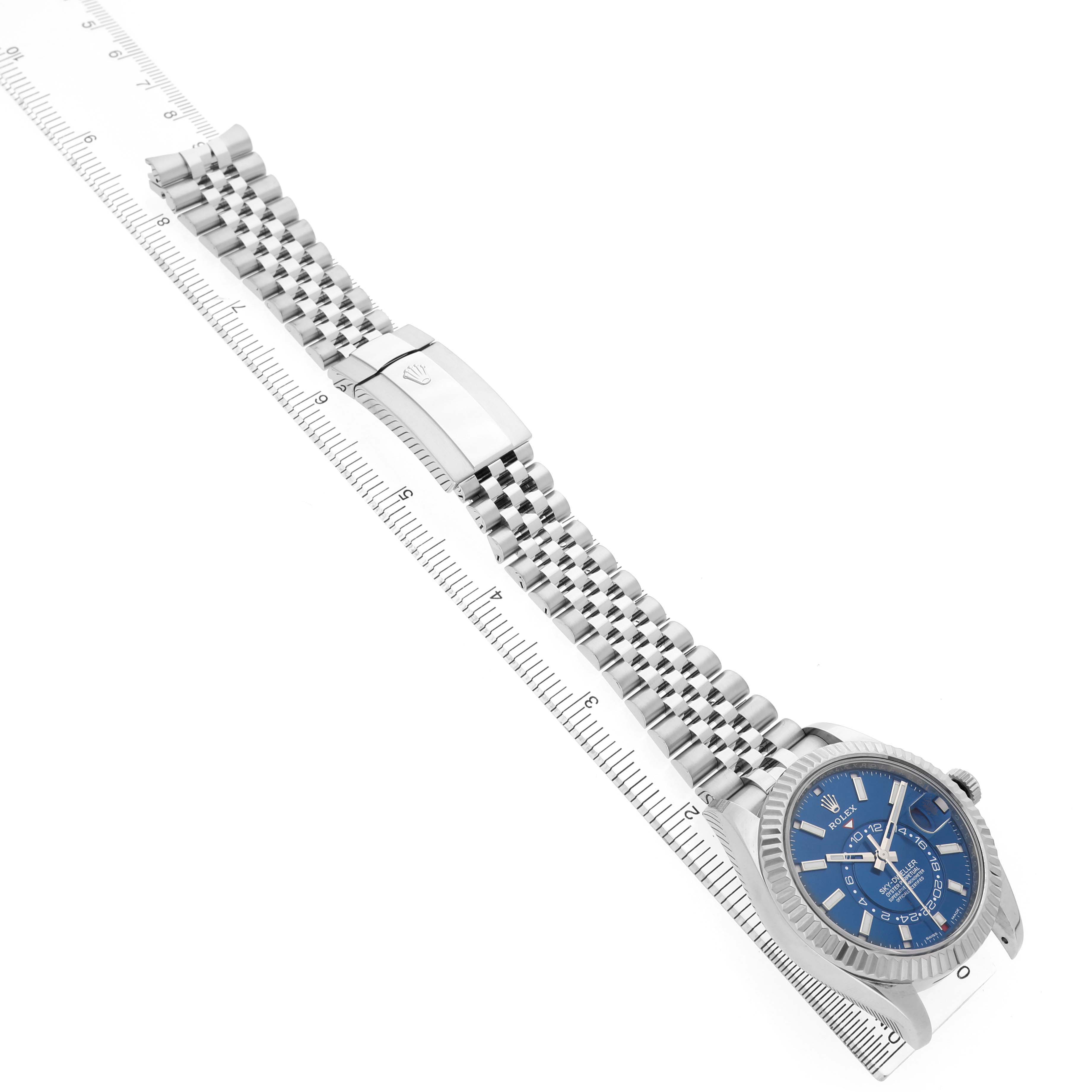 The Rolex Sky-Dweller 326934 Men's Stainless Steel Blue Dial watch is shown at an angle displaying the face, bracelet, and clasp, with a ruler for size reference.