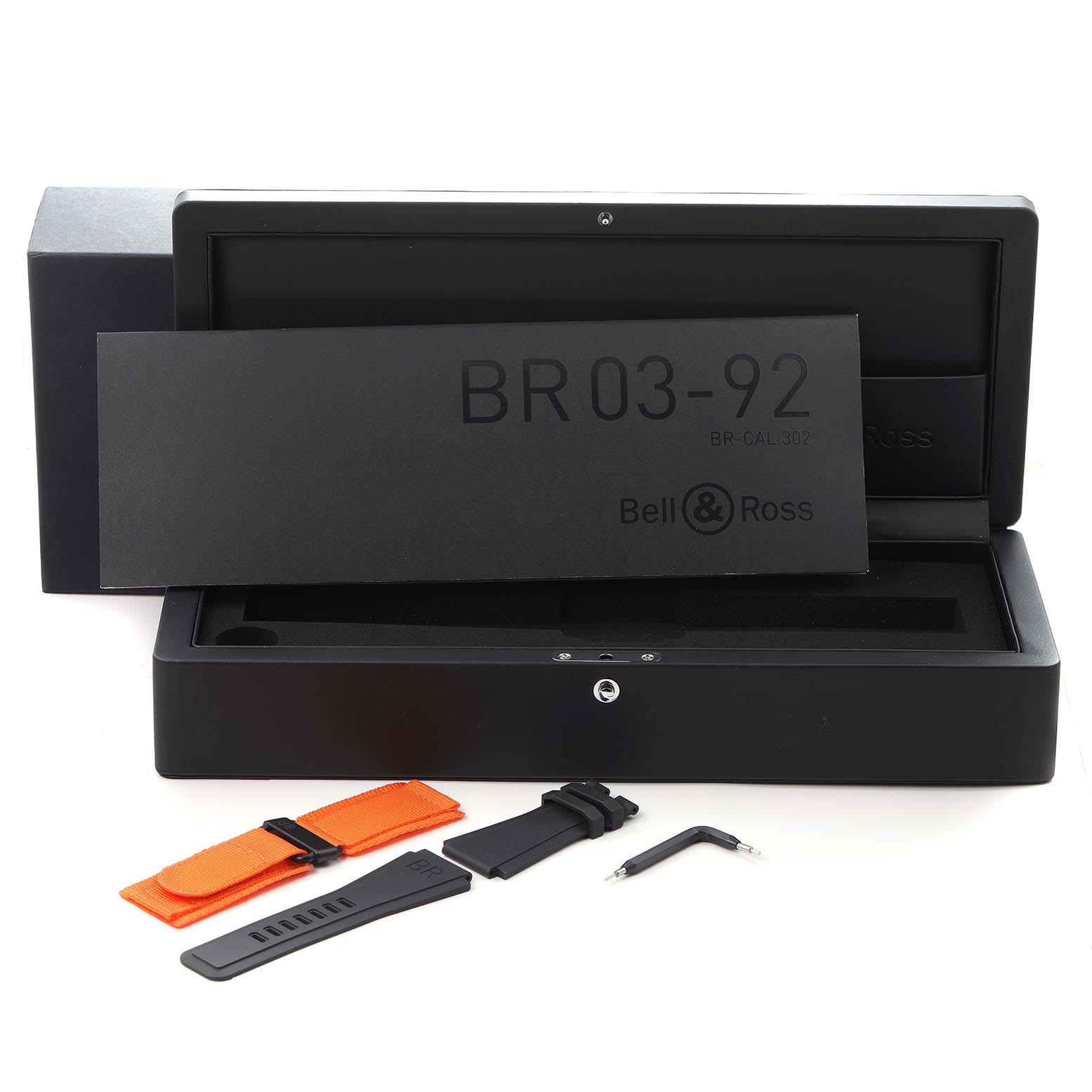 The image shows a Bell 
Ross Heritage BR03-92-CKA Men
s Ceramic Brown Dial BR03-92-CKA Men
s Ceramic Brown Dial BR 03-92 watch box, straps, and a tool, viewed from the front.