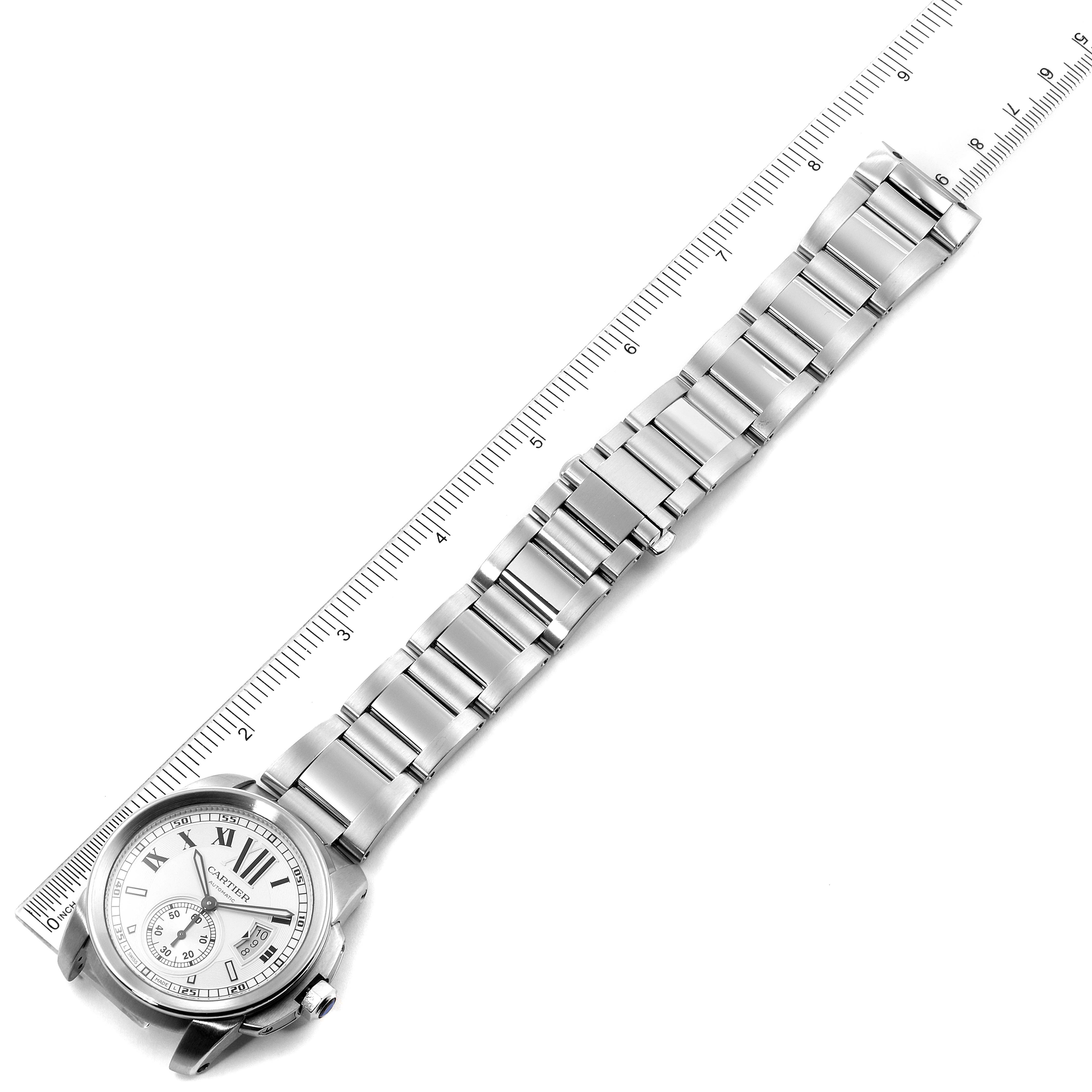 The Calibre de Cartier watch is shown from a top view, displaying its face, metal bracelet, and a ruler for scale.