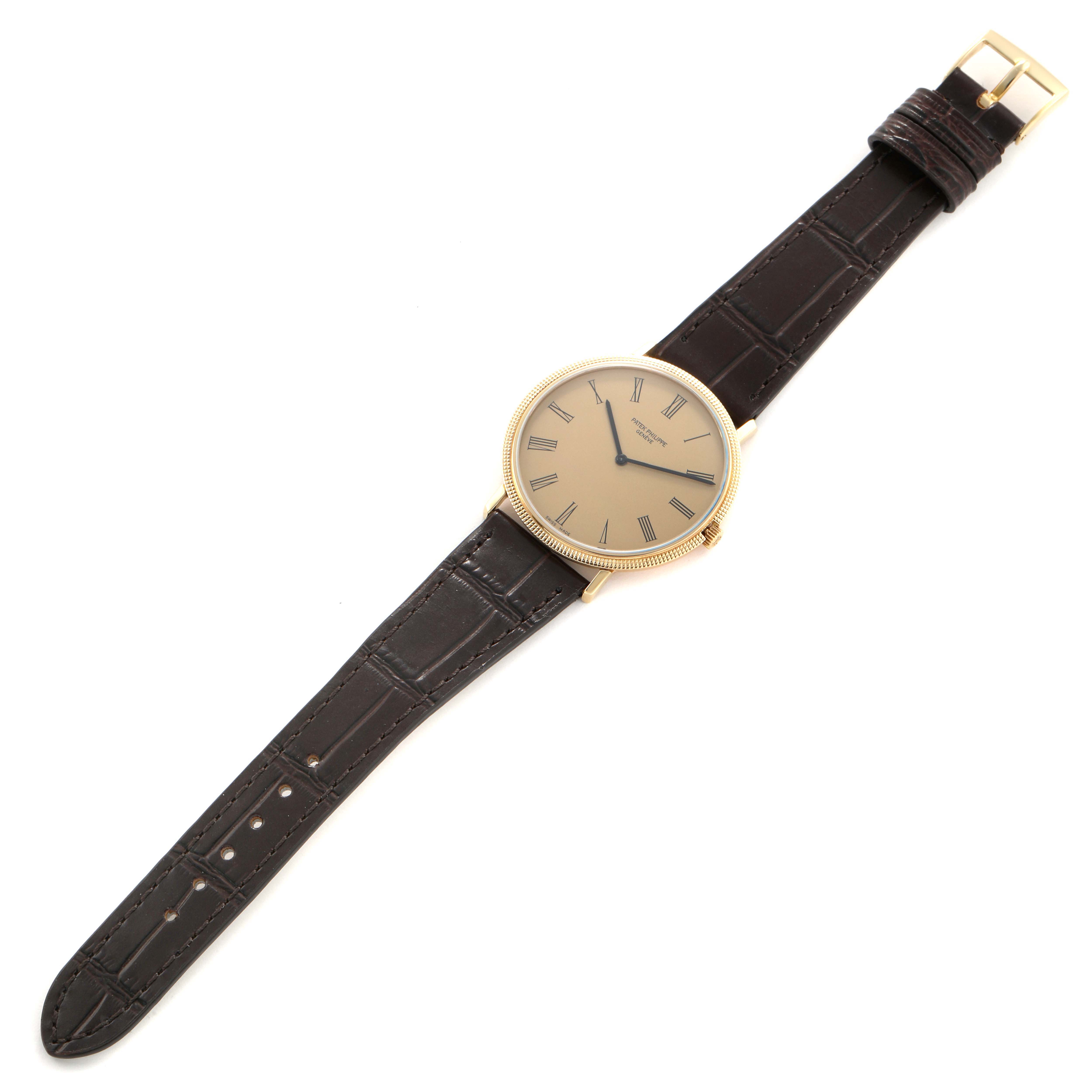The Patek Philippe Calatrava 3588J Men's Yellow Gold Beige Dial watch is shown from a top-down angle, displaying the face, brown leather strap, and gold buckle.