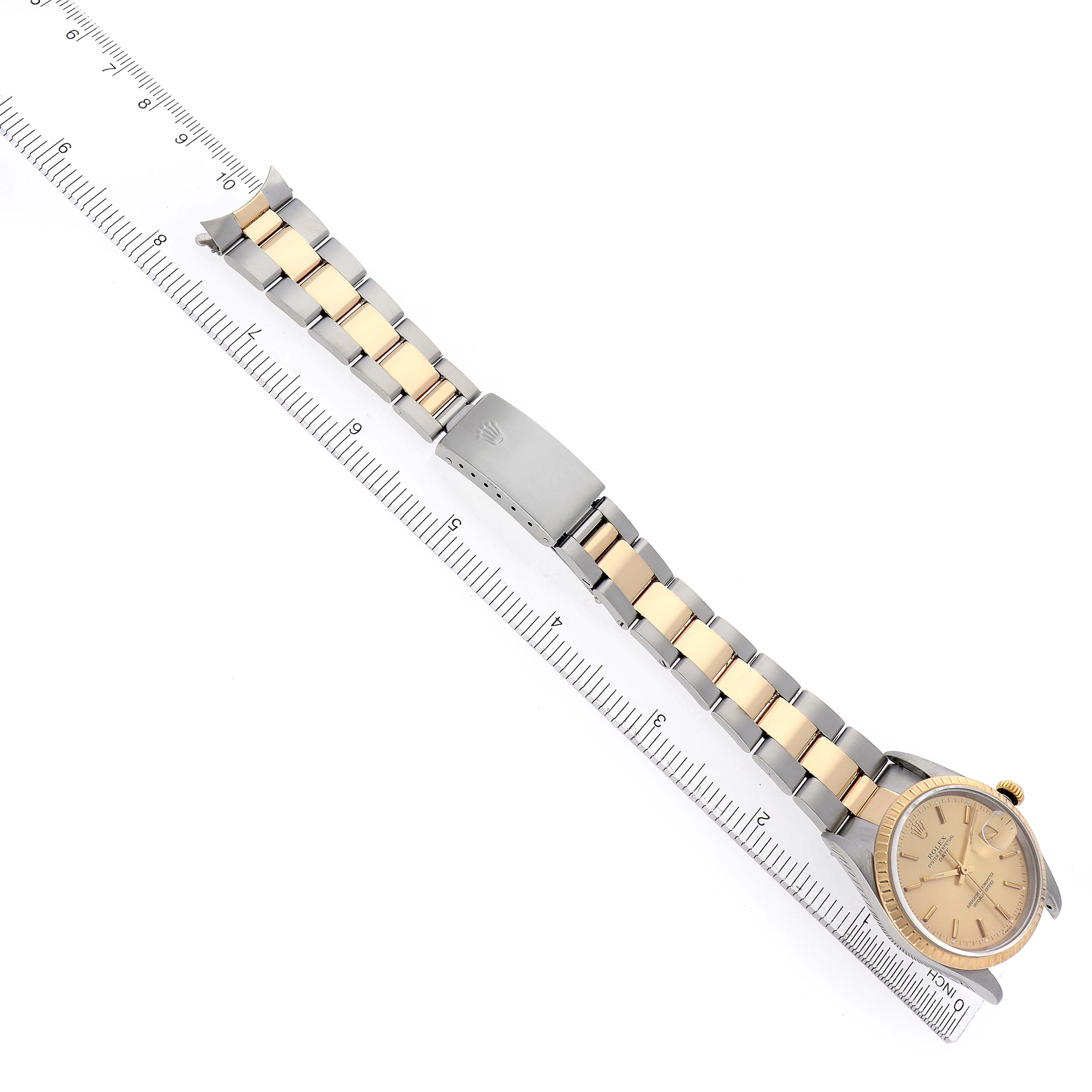 The Rolex Date 15223 Men
s Steel and Gold (two tone) Champagne Dial 15223 Men
s Steel and Gold (two tone) Champagne Dial watch is shown from a top-down angle, displaying the face, bracelet, and clasp alongside a ruler.