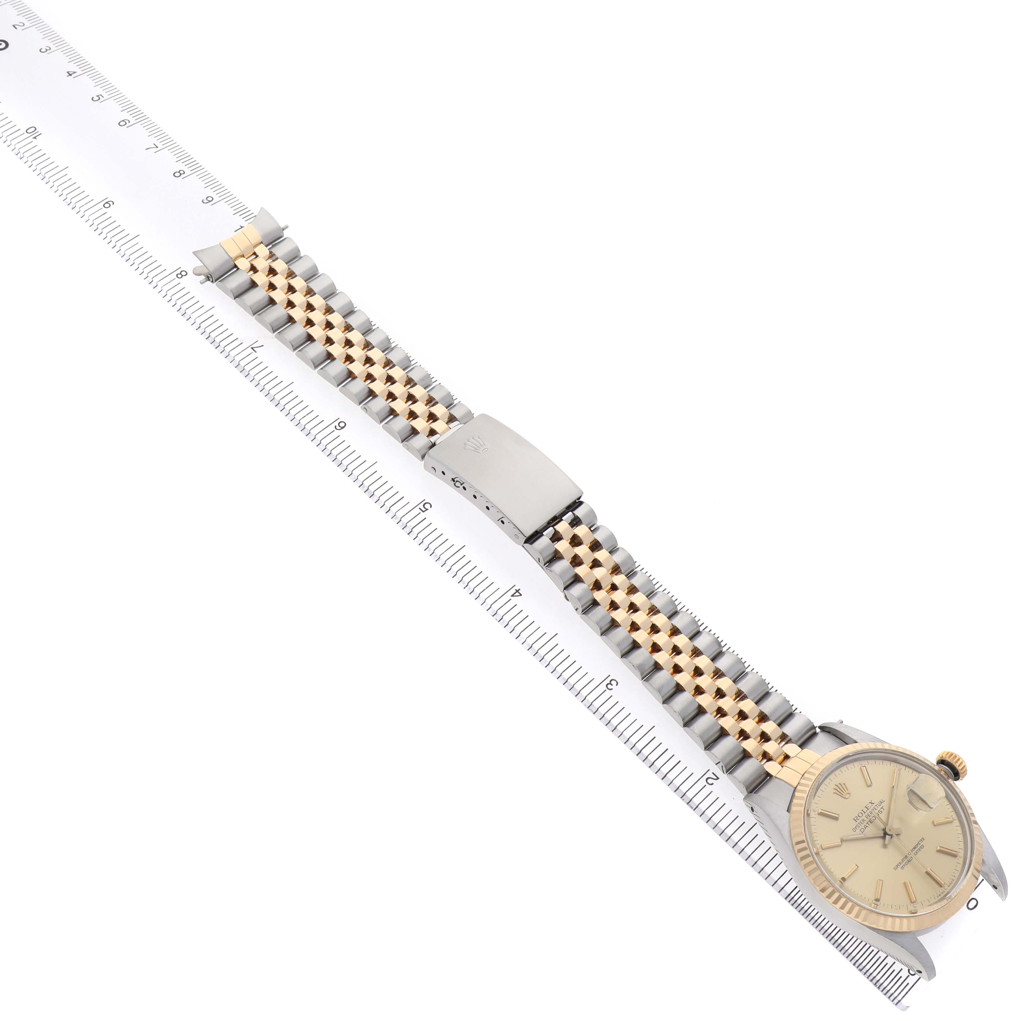 The Rolex Datejust 16013 Men's Steel and Gold (two tone) Champagne Dial watch is shown from an overhead angle, displaying the face, bracelet, and clasp alongside a ruler for scale.