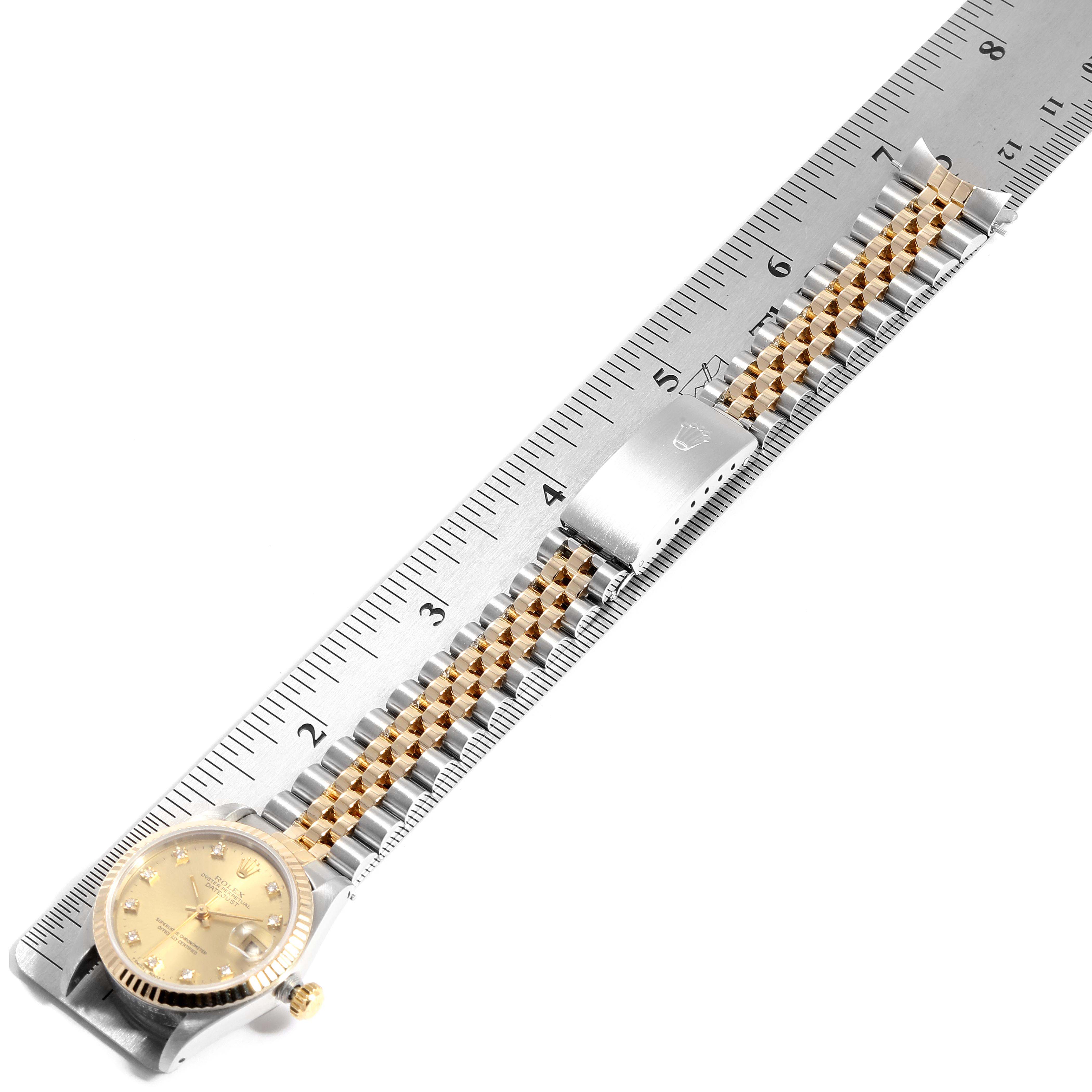 The image shows a Rolex Mid-Size 68273 Women
s Steel and Gold (two tone) Champagne Dial 68273 Women
s Steel and Gold (two tone) Champagne Dial watch positioned flat against a ruler, displaying its face, band, and clasp.