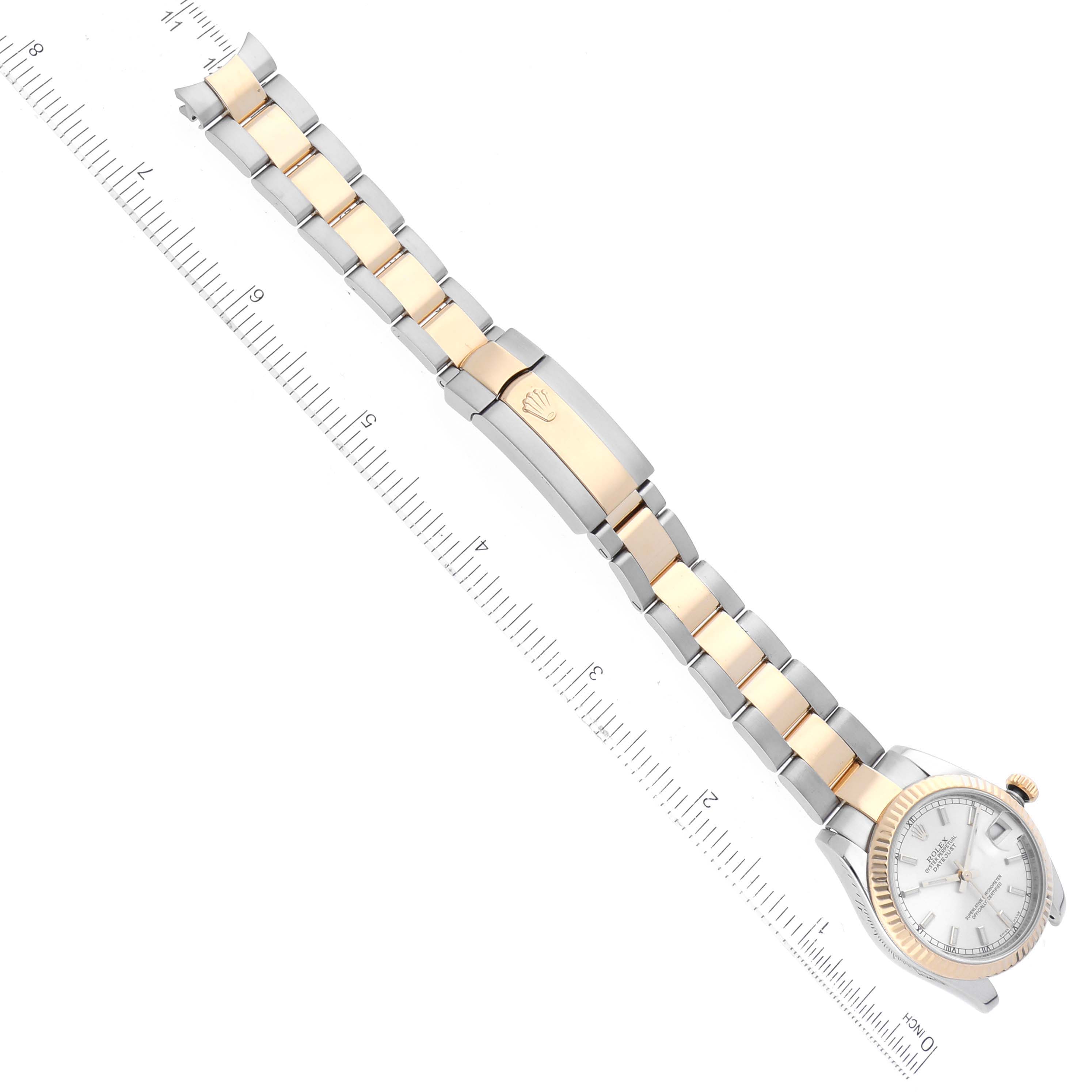 The image shows a Mid-Size Rolex watch laid flat with its crown, face, and bracelet visible, placed alongside a ruler for size reference.