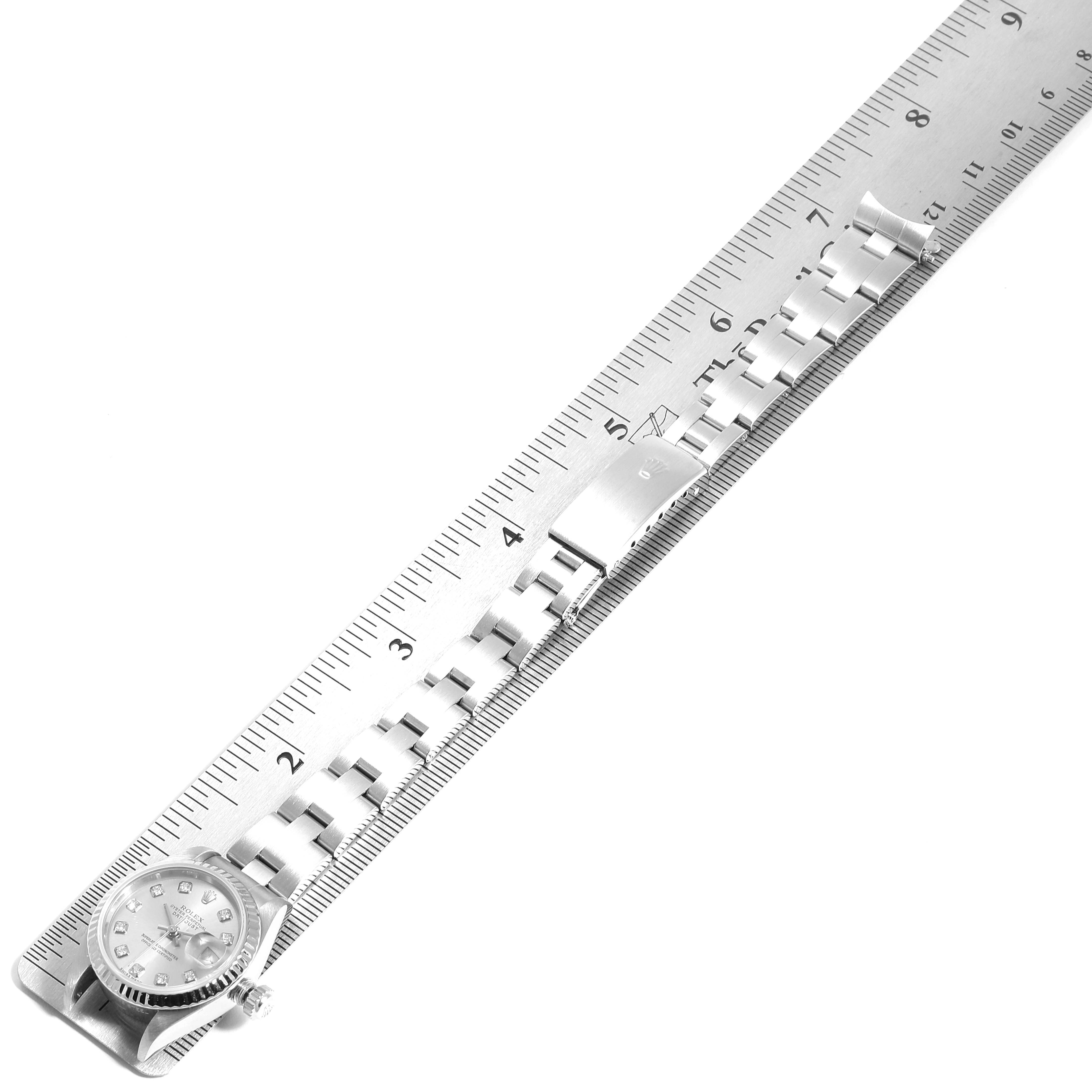 The image shows a top-down view of a Rolex Datejust 79174 Women
s Stainless Steel Silver Dial 79174 Women
s Stainless Steel Silver Dial watch and its metal bracelet placed alongside a ruler for measurement.
