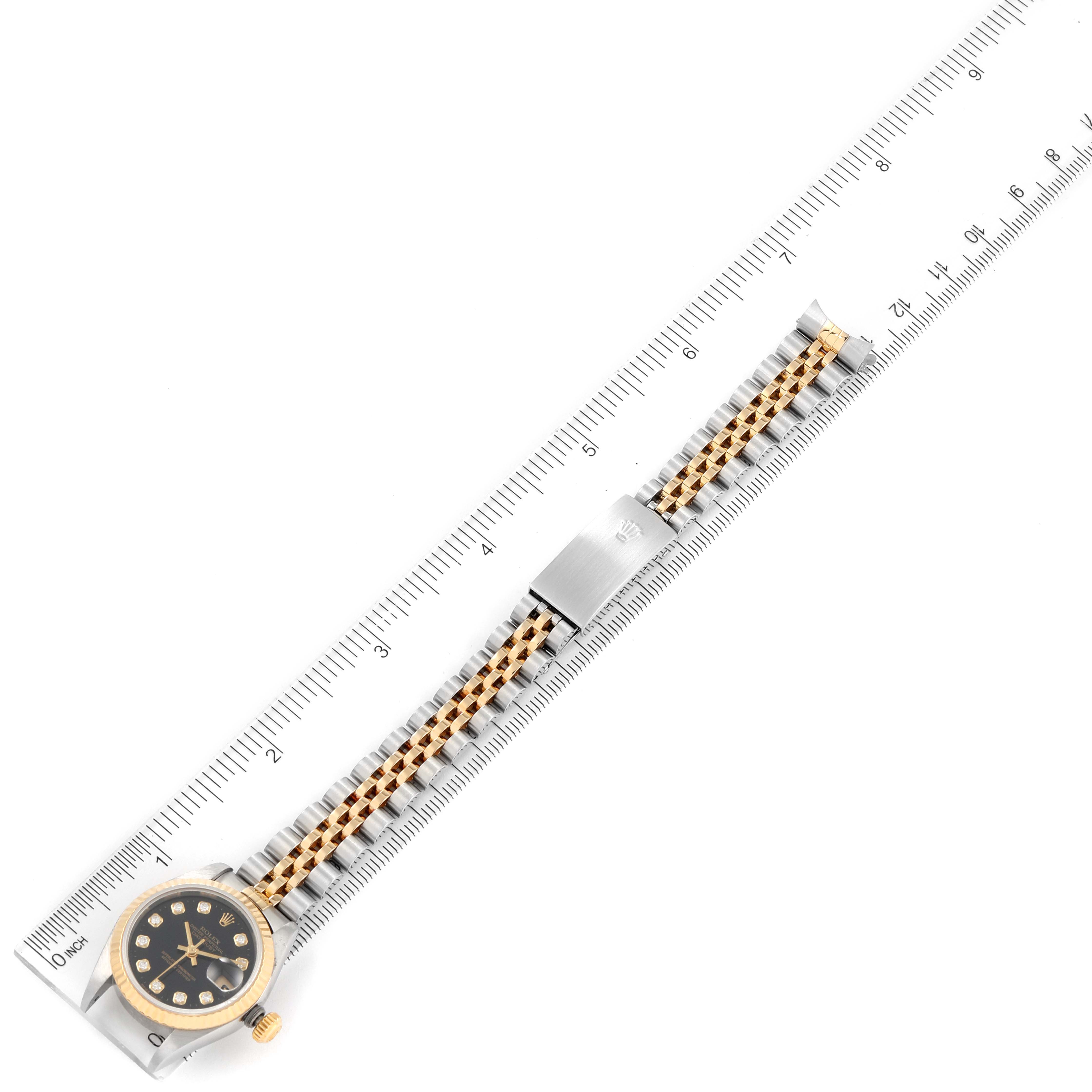 The Rolex Datejust 79173 Women's Steel and Gold (two tone) Black Dial 79173 Women's Steel and Gold (two tone) Black Dial watch is shown from an overhead angle, displaying the full bracelet and face alongside a ruler for scale.