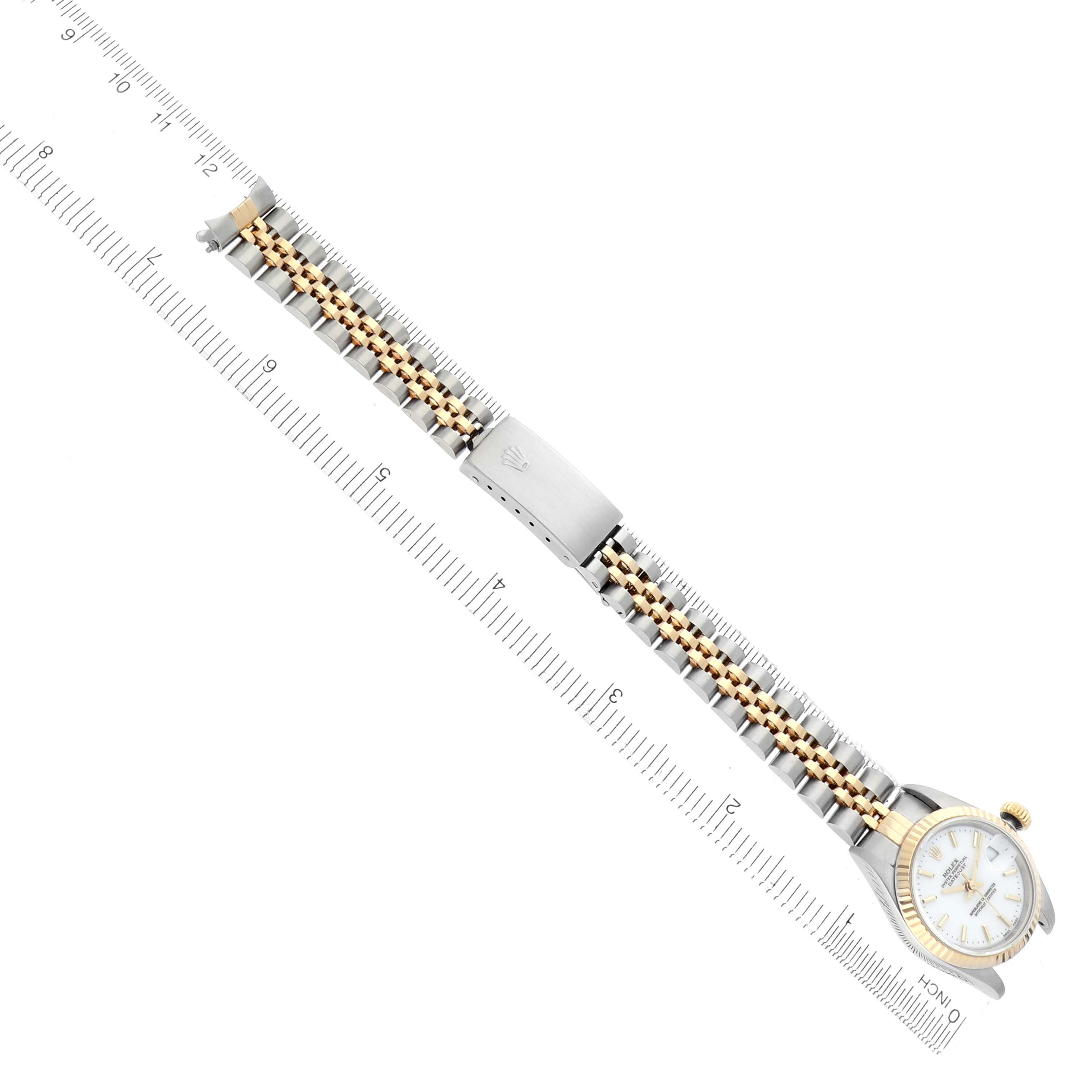 The image displays a Rolex Datejust 79173 Women
s Steel and Gold (two tone) White Dial 79173 Women
s Steel and Gold (two tone) White Dial watch laid flat, showing the full bracelet, clasp, and watch face from a top-down angle alongside a ruler.