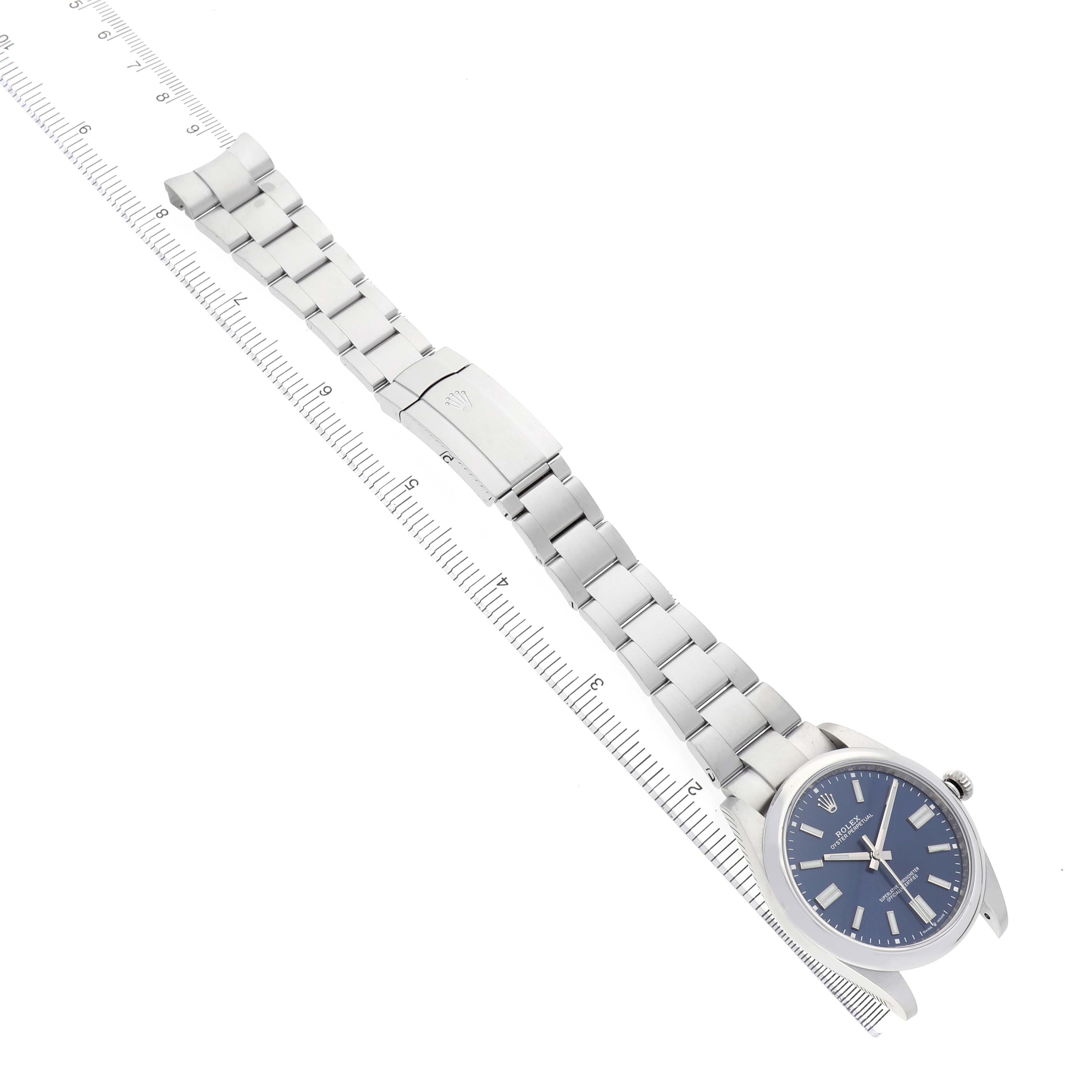 The Rolex Oyster Perpetual 124300 Men's Stainless Steel Blue Dial is shown angled diagonally, displaying the full watch and bracelet alongside a ruler for size reference.