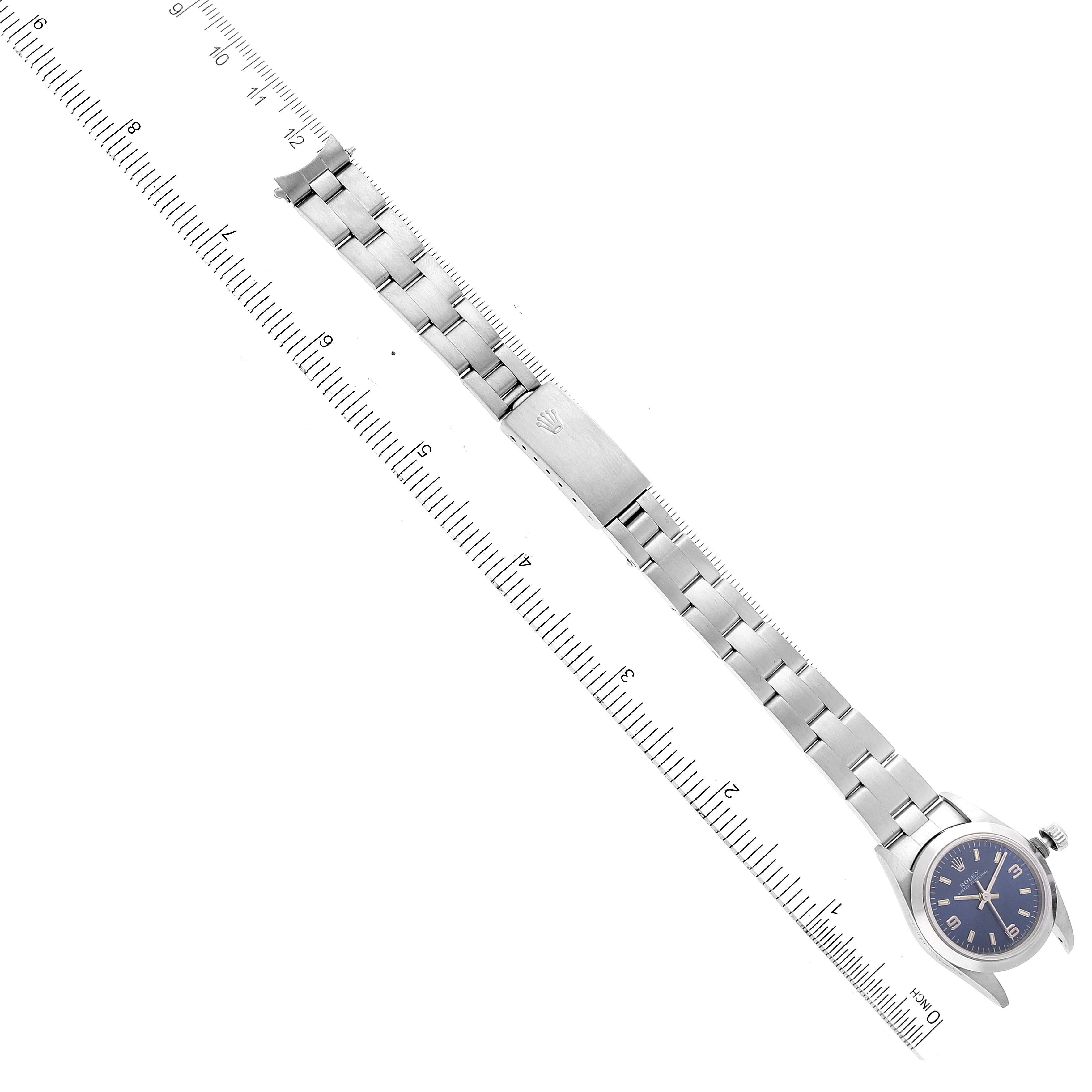 The image shows a flat lay of a Rolex Oyster Perpetual 67180 Women's Stainless Steel Blue Dial 67180 Women's Stainless Steel Blue Dial watch, highlighting its bracelet, clasp, and face with a ruler for scale.