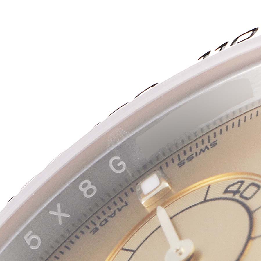 The image shows a close-up angle of the Rolex Daytona 116503 Men
s Steel and Gold (two tone) Champagne Dial 116503 Men
s Steel and Gold (two tone) Champagne Dial watch, highlighting the bezel, part of the dial, and an index marker.