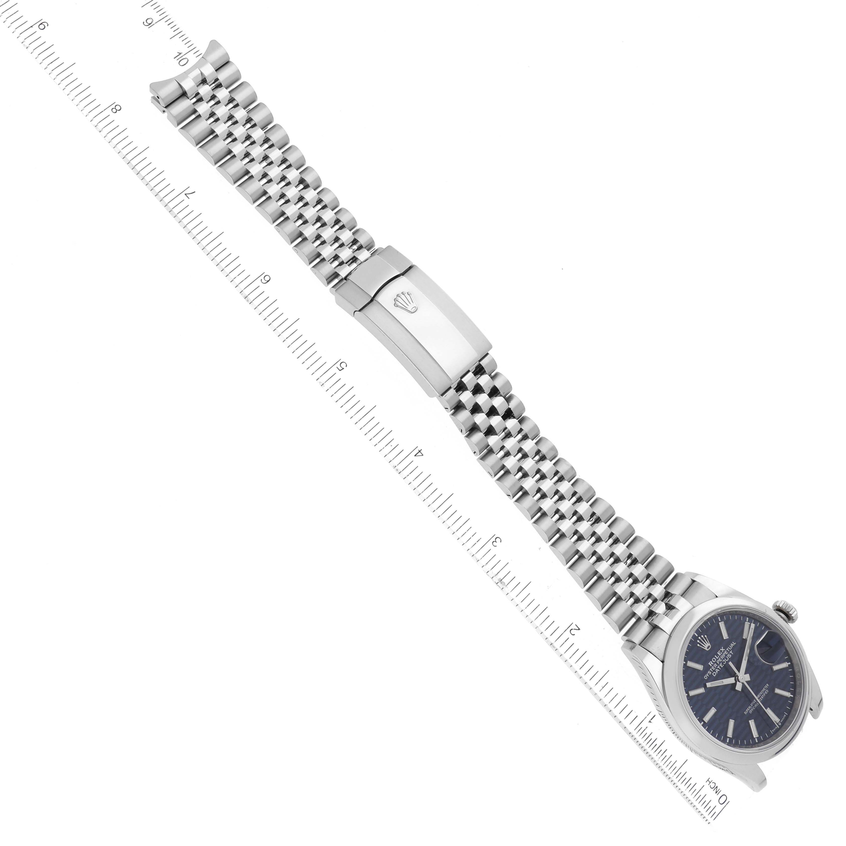 The image shows a Rolex Datejust 126200 Men's Stainless Steel Blue Dial 126200 Men's Stainless Steel Blue Dial watch from an overhead angle, highlighting its face, clasp, and bracelet against a ruler for scale.