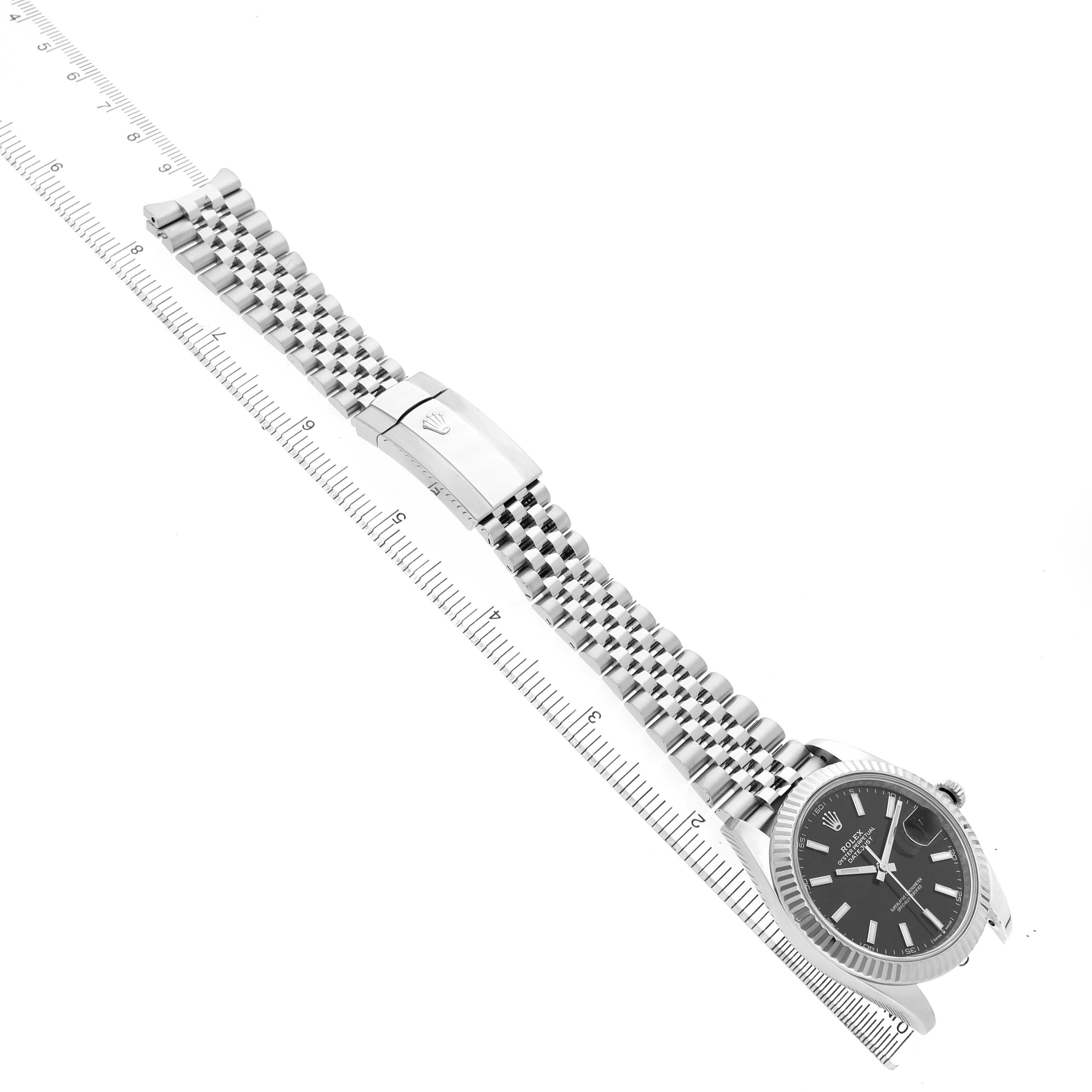 The image shows a Rolex Datejust 41 M126334-0018 Men's Stainless Steel Black Dial laid flat with its Jubilee bracelet and clasp visible, alongside a ruler for scale.