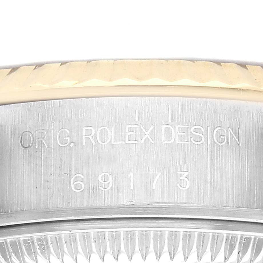 The image shows the side of a Rolex Datejust 69173 Women
s Steel and Gold (two tone) Champagne Dial 69173 Women
s Steel and Gold (two tone) Champagne Dial watch case with engravings and part of the fluted bezel visible.