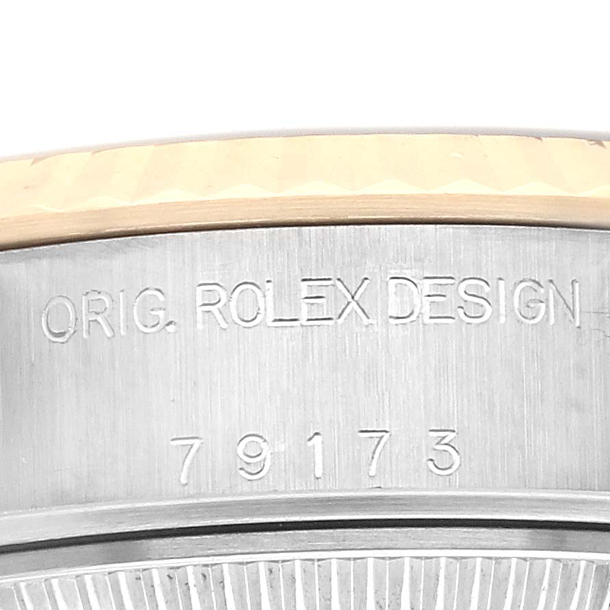 The image shows an angled close-up of the Rolex Datejust 79173 Women
s Steel and Gold (two tone) White Dial 79173 Women
s Steel and Gold (two tone) White Dial watch
s bezel and engraved model number.