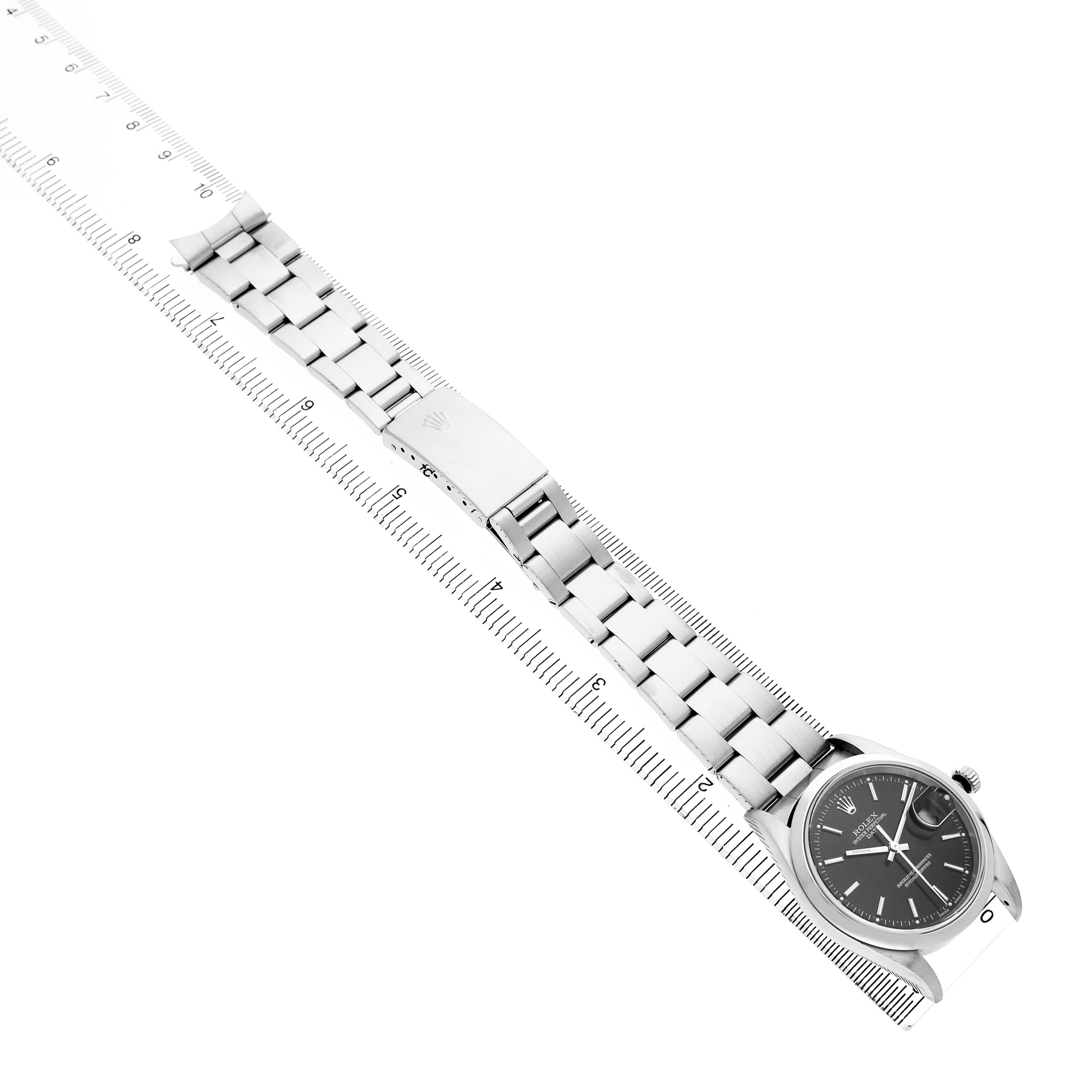 The Rolex Oyster Perpetual 15200 Men's Stainless Steel Black Dial watch is shown diagonally, displaying the bracelet, clasp, and face with a ruler for scale.
