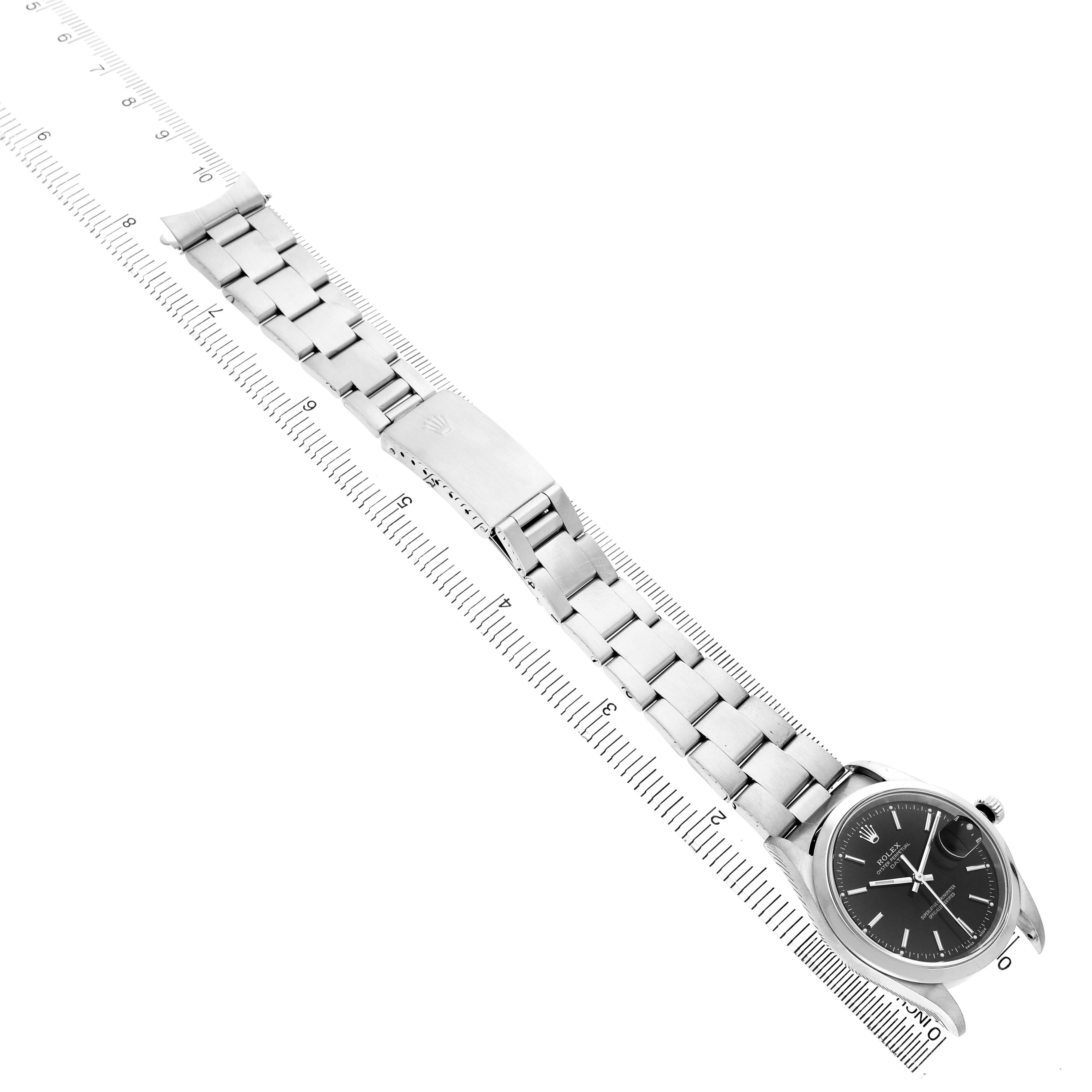The Rolex Date 15200 Men's Stainless Steel Black Dial model watch is shown from a top view, highlighting the face, bracelet, and clasp alongside a ruler for scale.